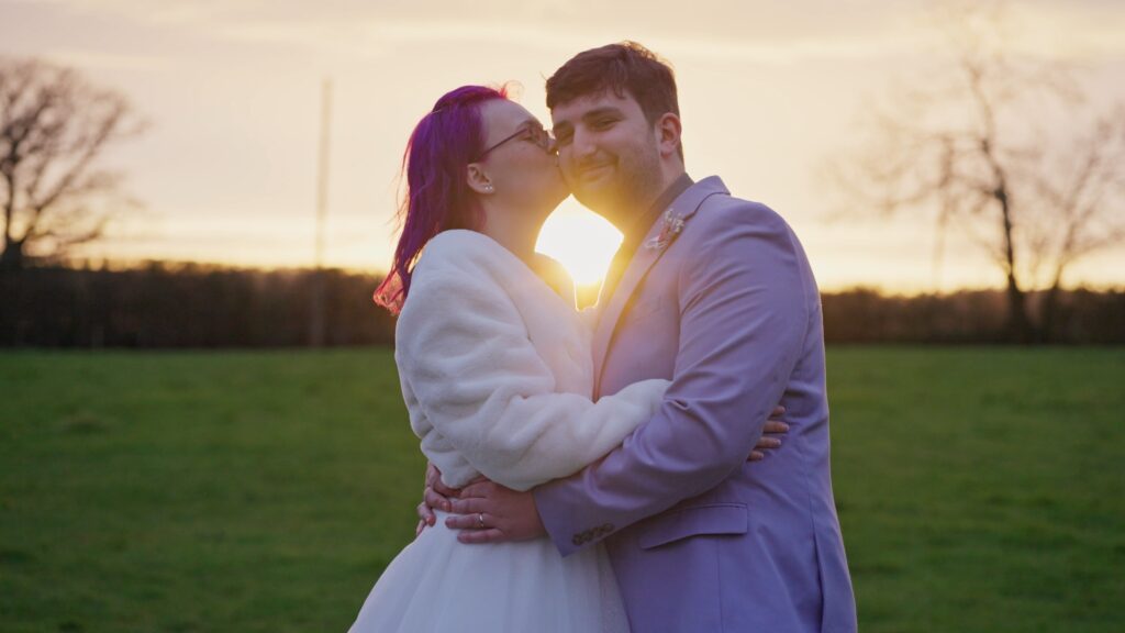 Wedding couple being photographed against a sunset with it coming through the middle of their heads.