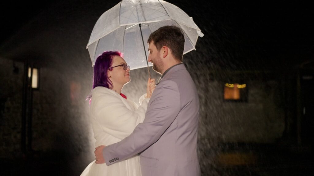 Bride & Groom under an umbrella while it is raining for a moody photograph.