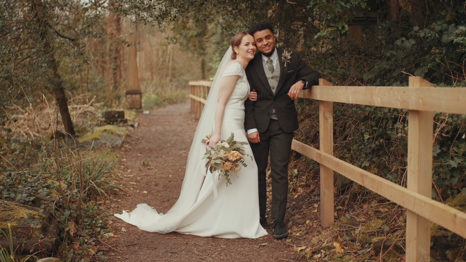 : Bride leaning into the groom with warm smiles, surrounded by forest greenery — a natural moment captured by a documentary wedding videographer.