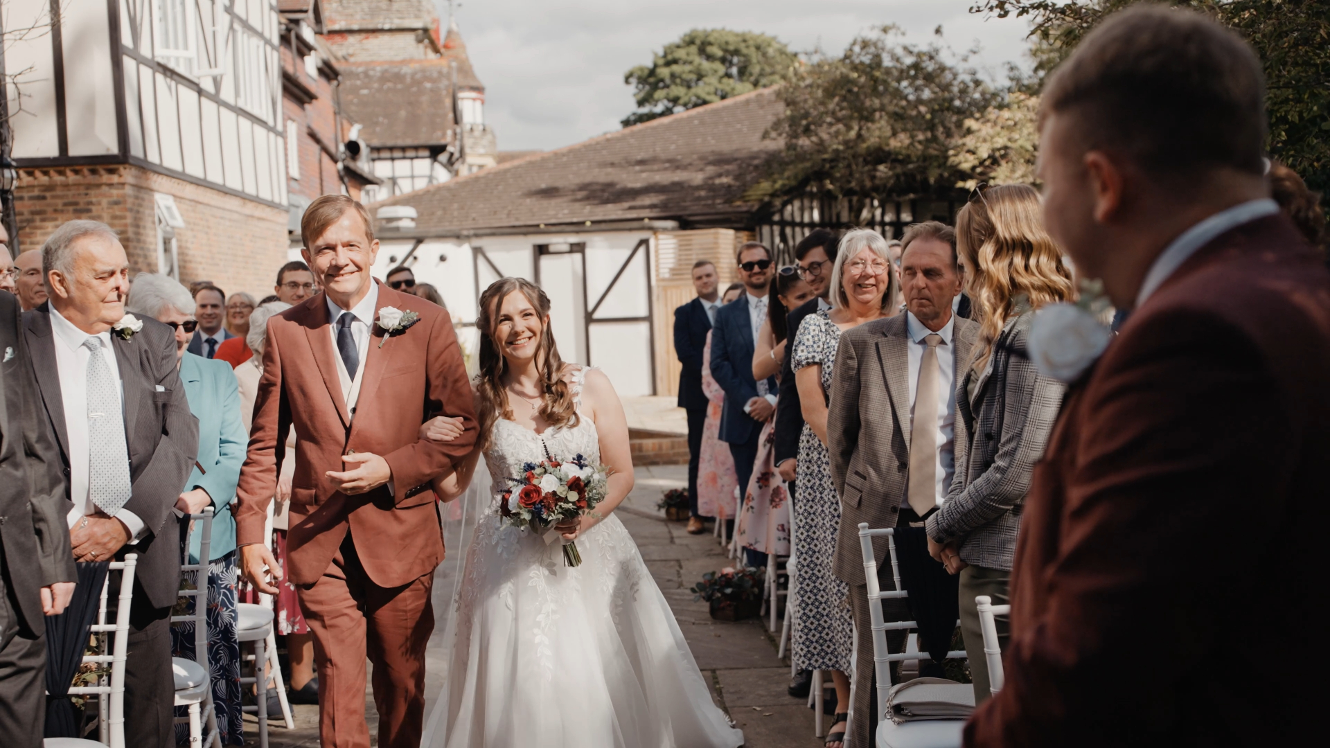 Father of the bride walking his daughter down the aisle as smiling guests look on — a joyful moment to capture in your wedding video by a Somerset wedding videographer
