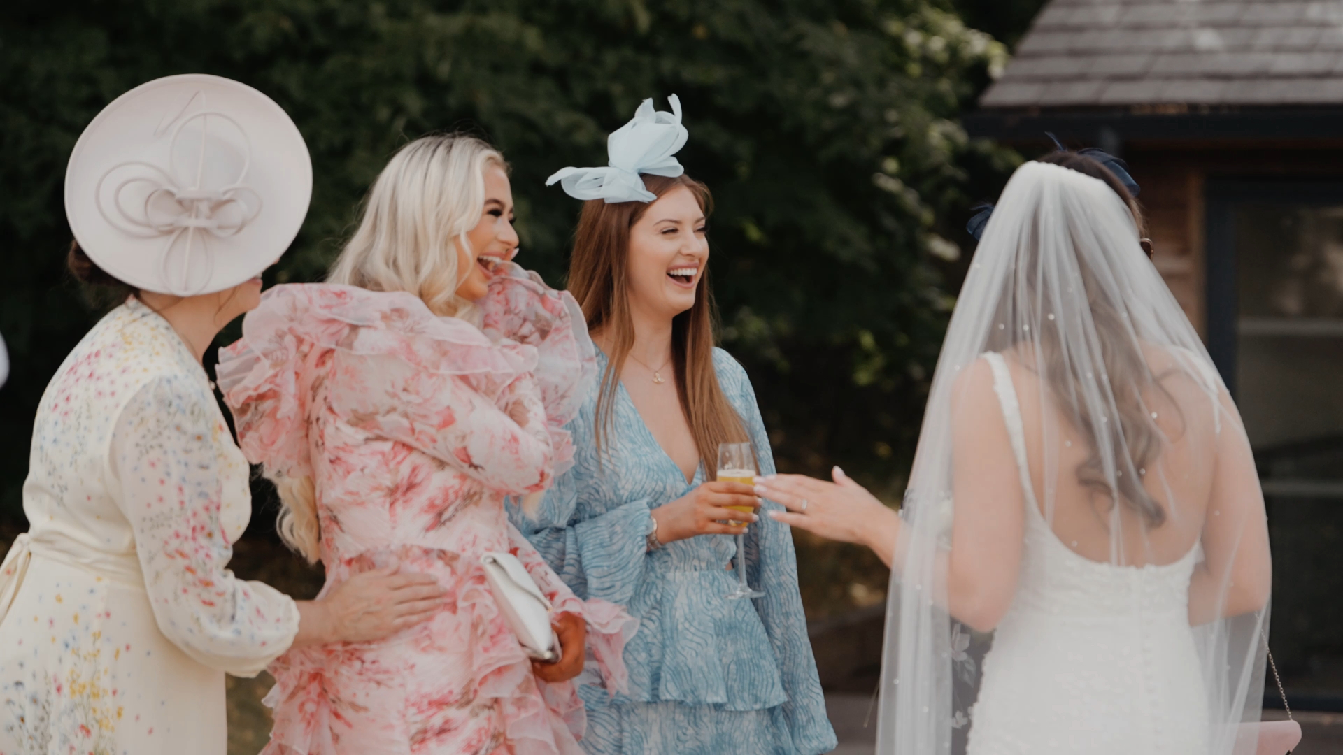 Two well-dressed wedding guests, one in a blue floral dress and the other in a pink dress, chat warmly with the bride, reflecting the 2025 wedding trend of stylish guest attire and candid interactions.