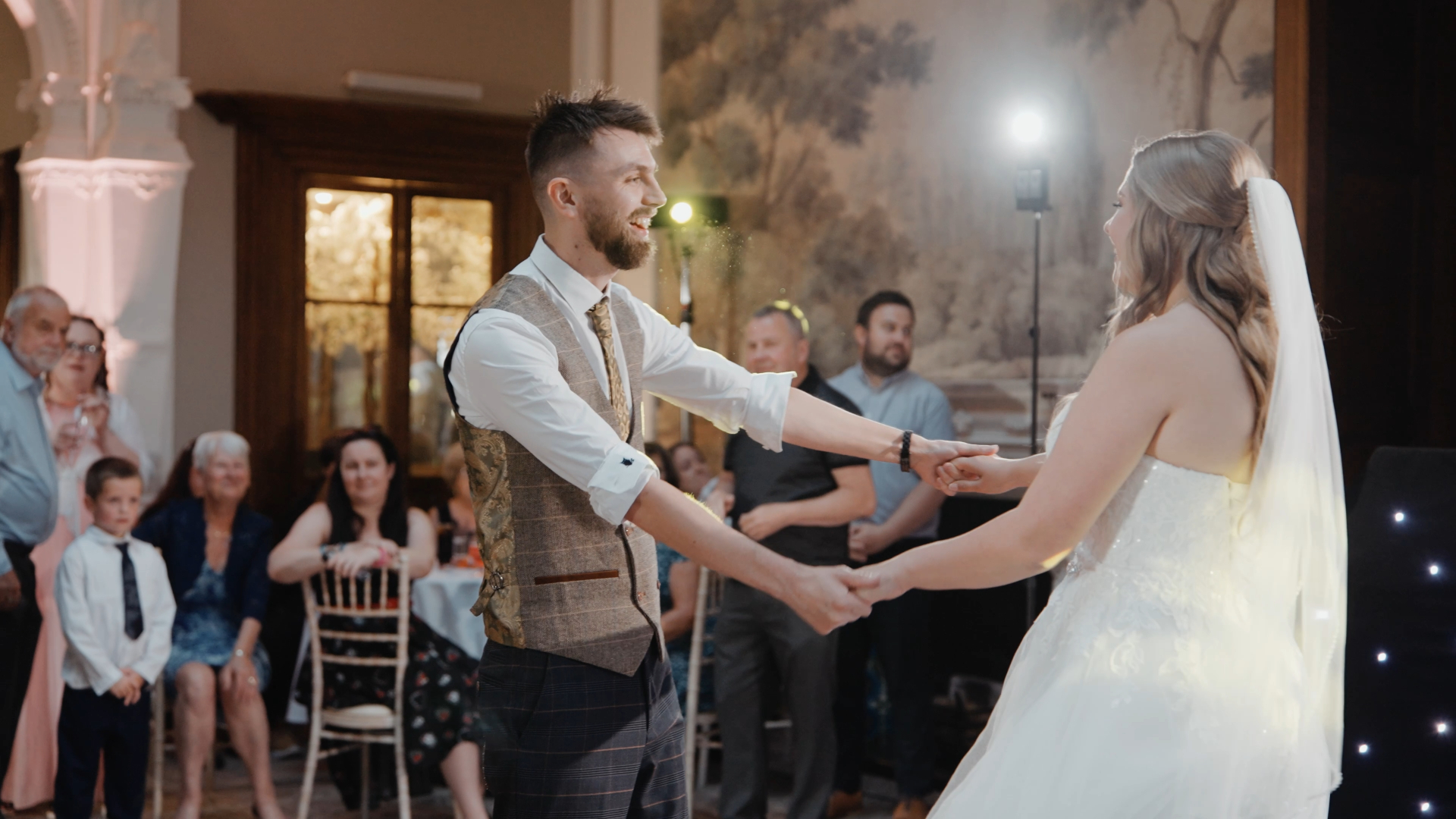 Bride and groom dancing hand in hand, with guests watching joyfully — a candid moment captured by a documentary wedding videographer.