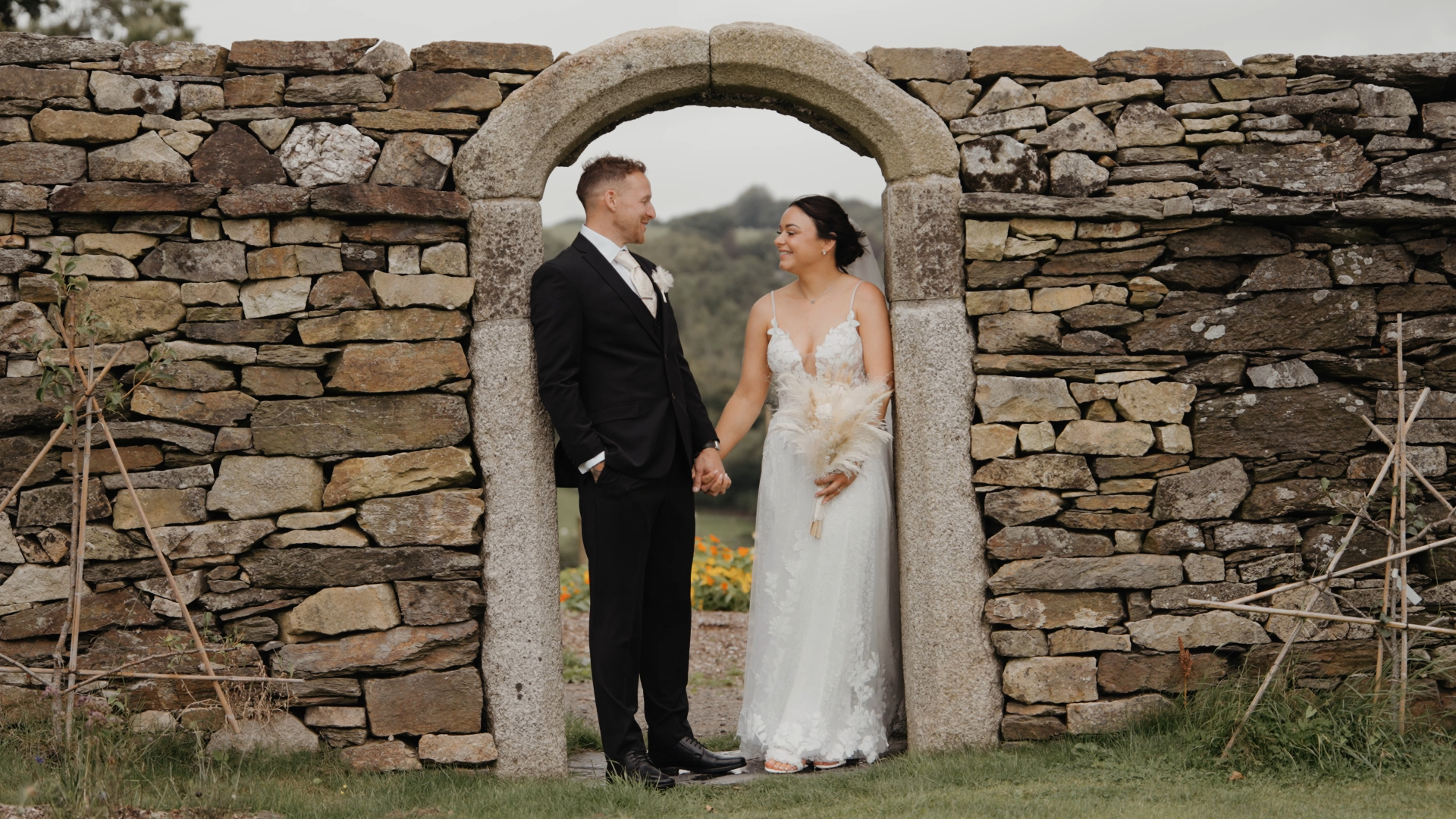 Bride and groom standing under a stone arch, gazing at each other with love — a quiet moment filmed by a documentary wedding videographer.
