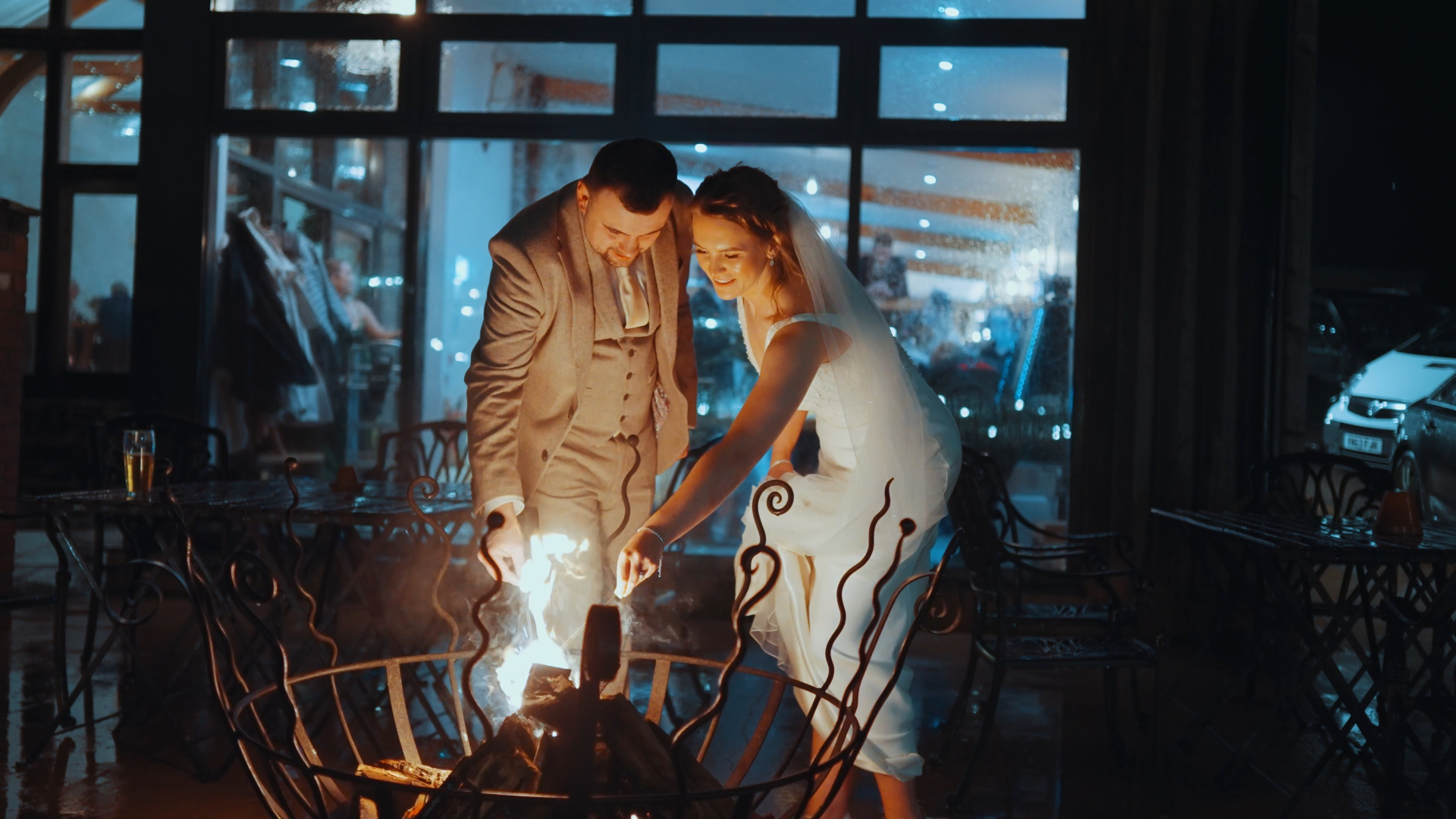 Bride and groom lighting a wood fire together, sharing an intimate, cozy moment during their wedding, as seen through a documentary wedding videographer’s lens.