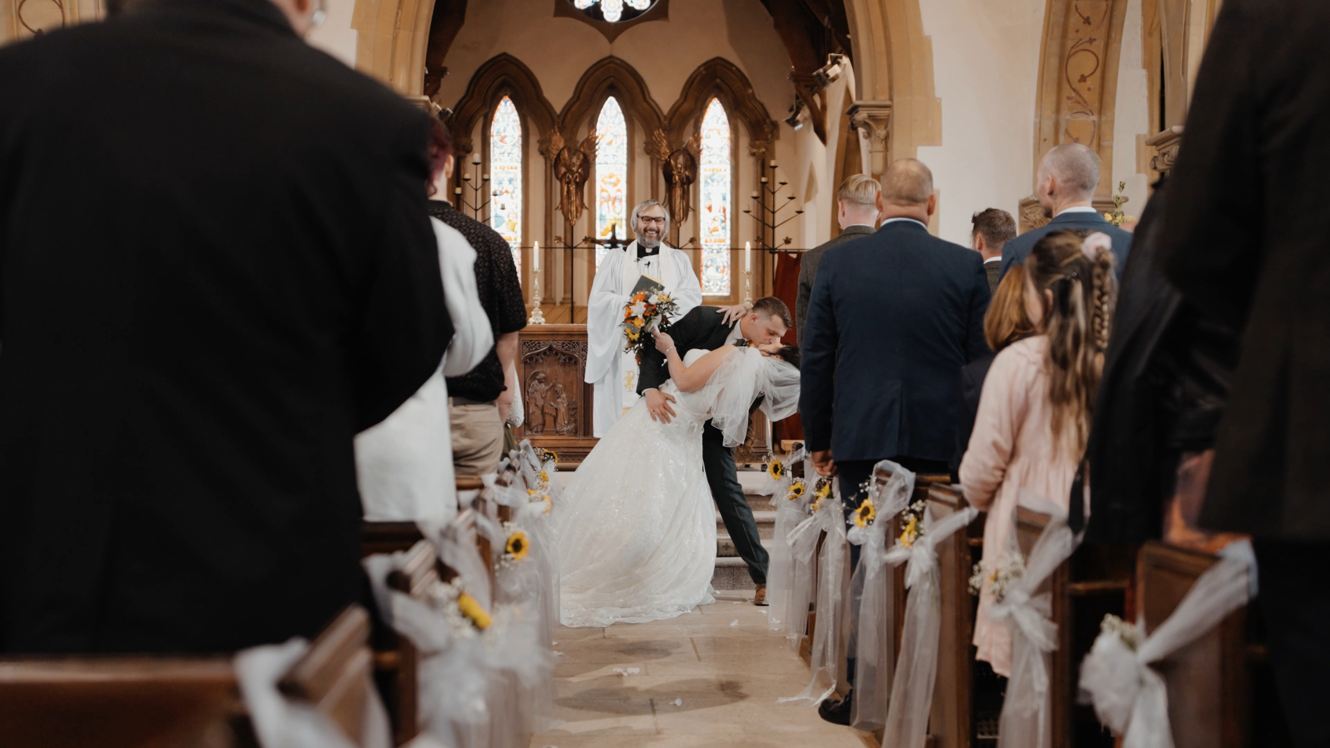 A playful and romantic moment captured by a wedding videographer as the groom dips the bride for a kiss in front of cheering guests after the ceremony.