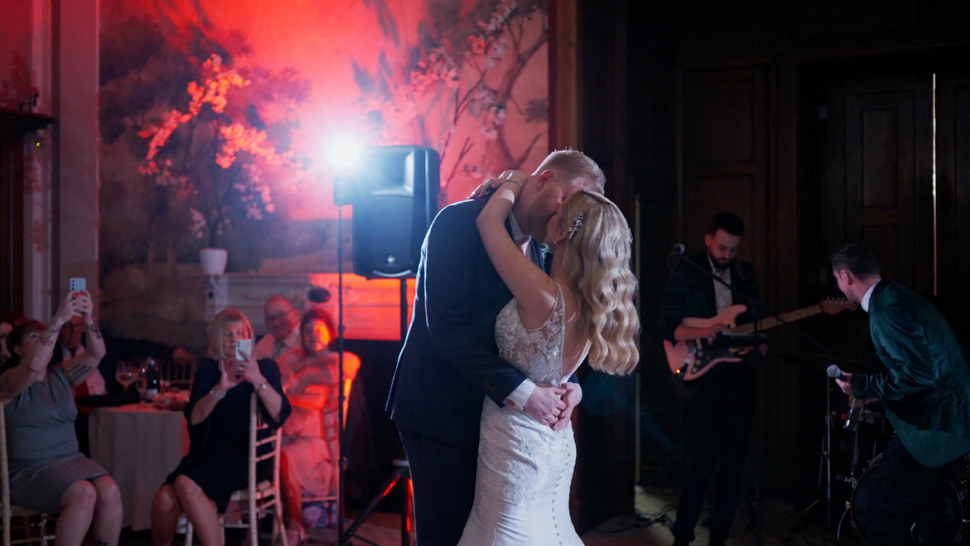 Bride and groom sharing a kiss on the dance floor, backlit by orange light — a cinematic moment captured by a documentary wedding videographer.