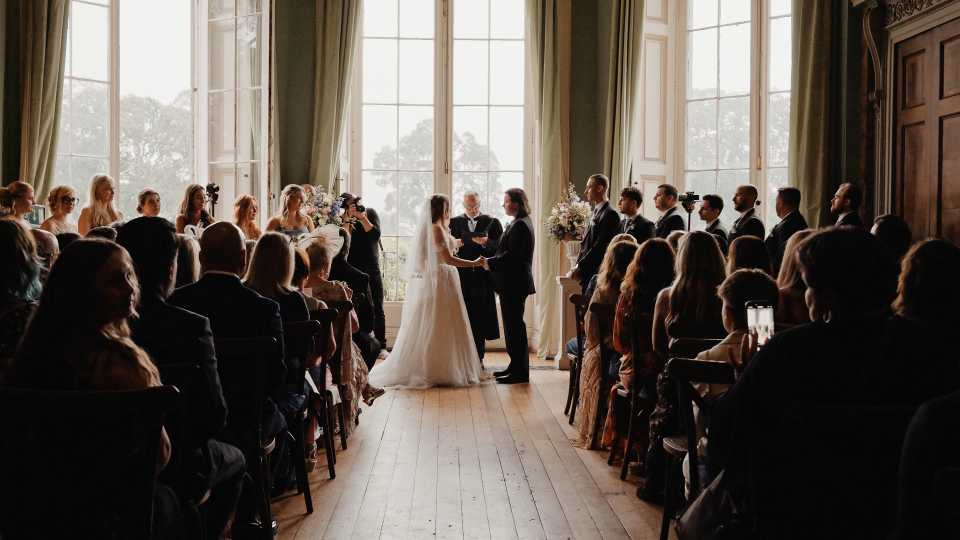 The bride and groom stand hand in hand, facing each other in front of the altar as their guests look on. The moment is filled with love and anticipation during the wedding ceremony.