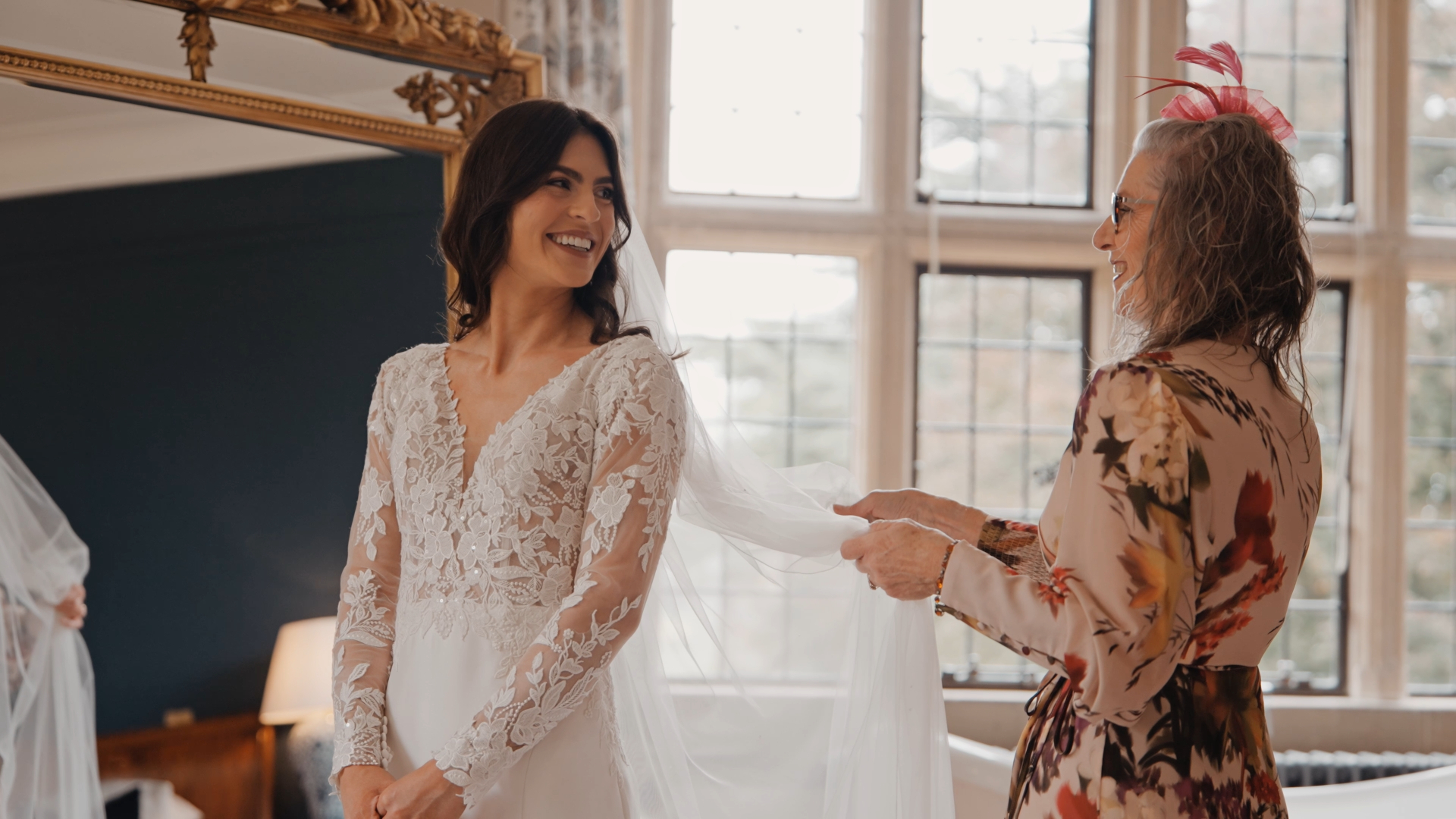 Bride in a floral wedding dress smiles at her mother, who is gently fixing her veil—capturing a heartfelt moment that highlights one of the top wedding trends in 2025: floral-patterned bridal gowns blending tradition with modern elegance.