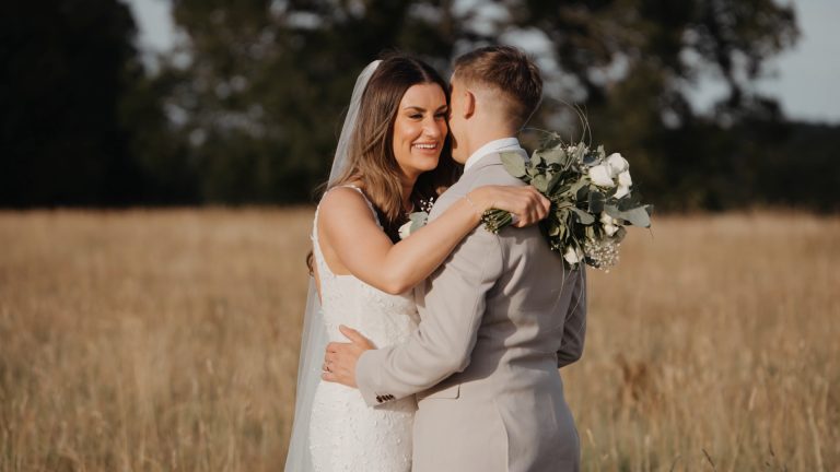 Bride and groom hugging in a sunlit field while bride holds bouquet — a romantic moment to capture in your wedding video