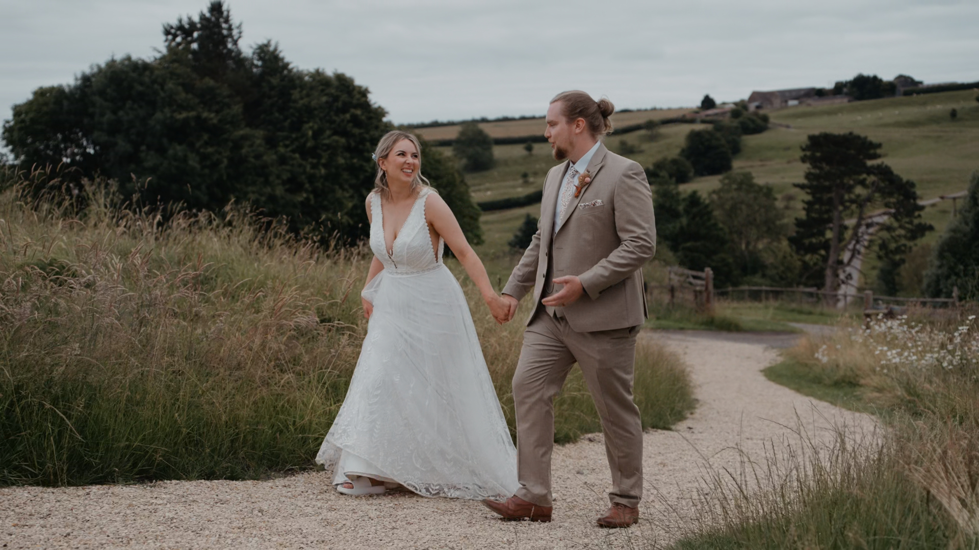 Bride and groom walking hand in hand on a pavement beside a field