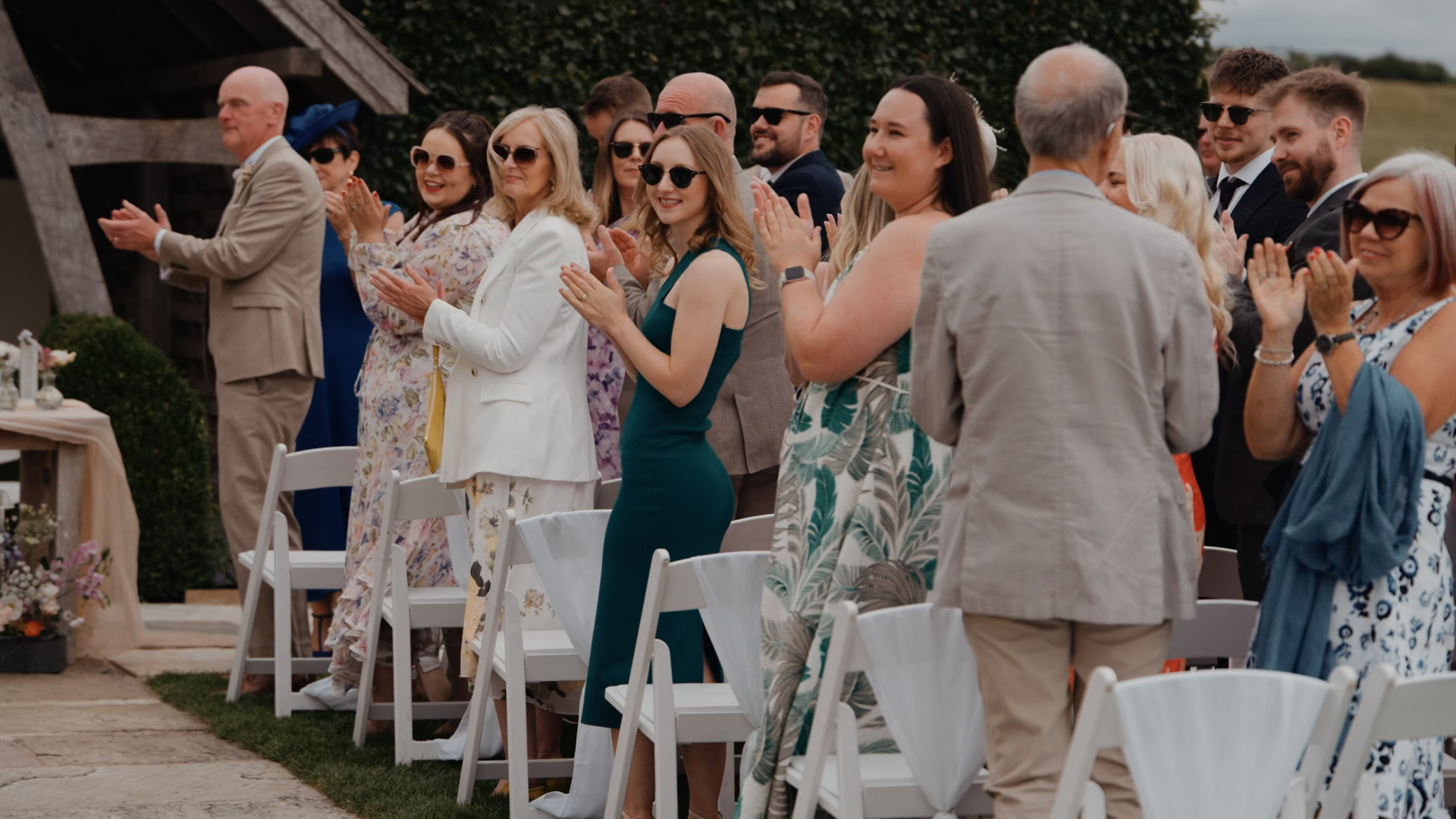 Well-dressed wedding guests clapping while looking toward the aisle, showcasing one of the standout wedding trends in 2025—elevated guest attire that complements the event’s elegant aesthetic.
