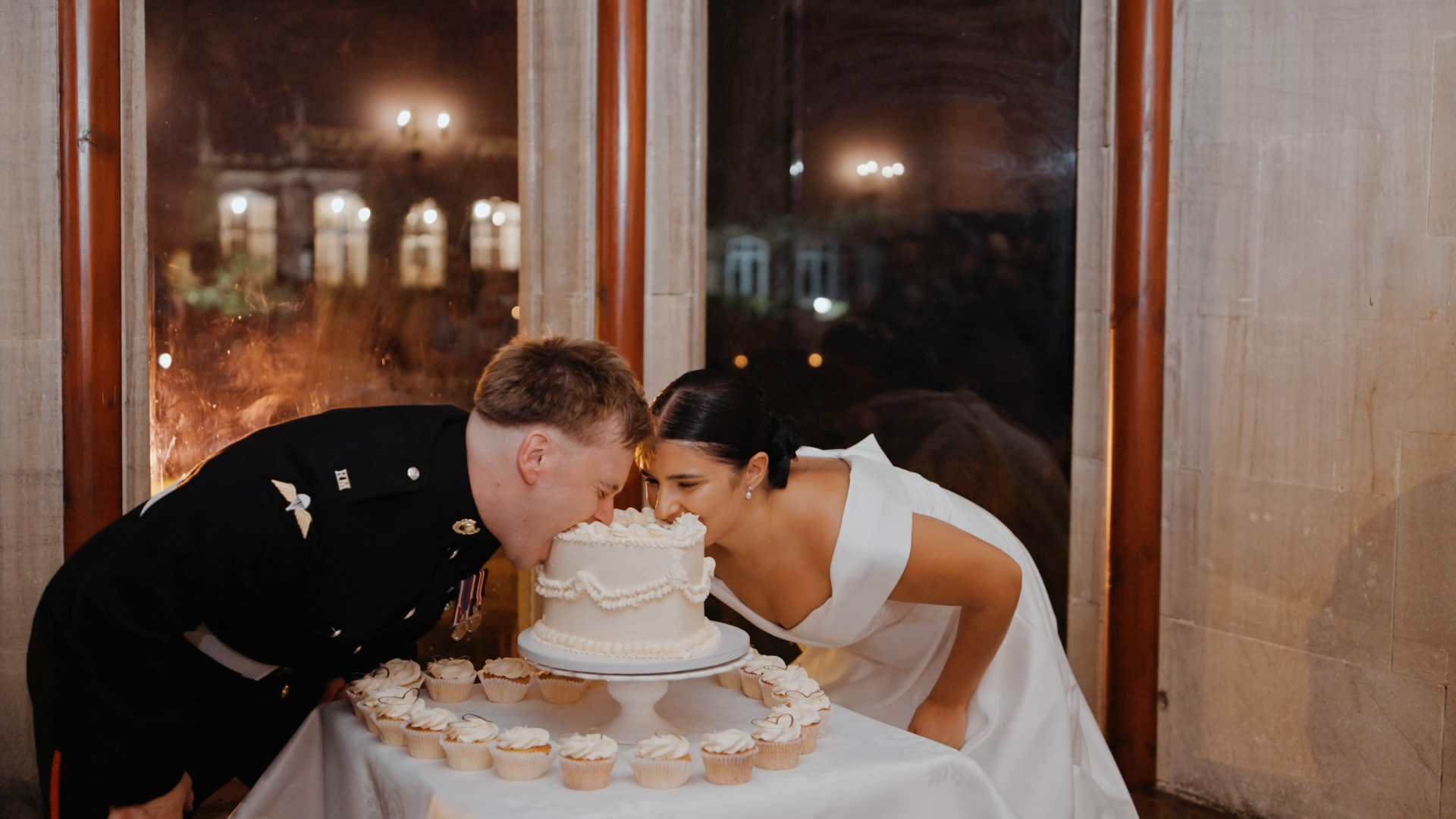 Bride and groom playfully biting opposite ends of their Lambeth cake, capturing one of the fun and trending moments for weddings in 2025.