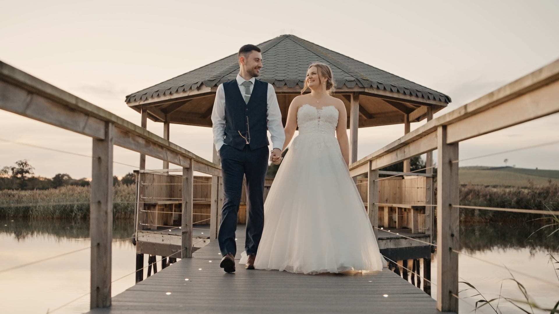 Somerset wedding videographer captures bride and groom smiling at each other on the bridge at Quantock Lakes, surrounded by nature.