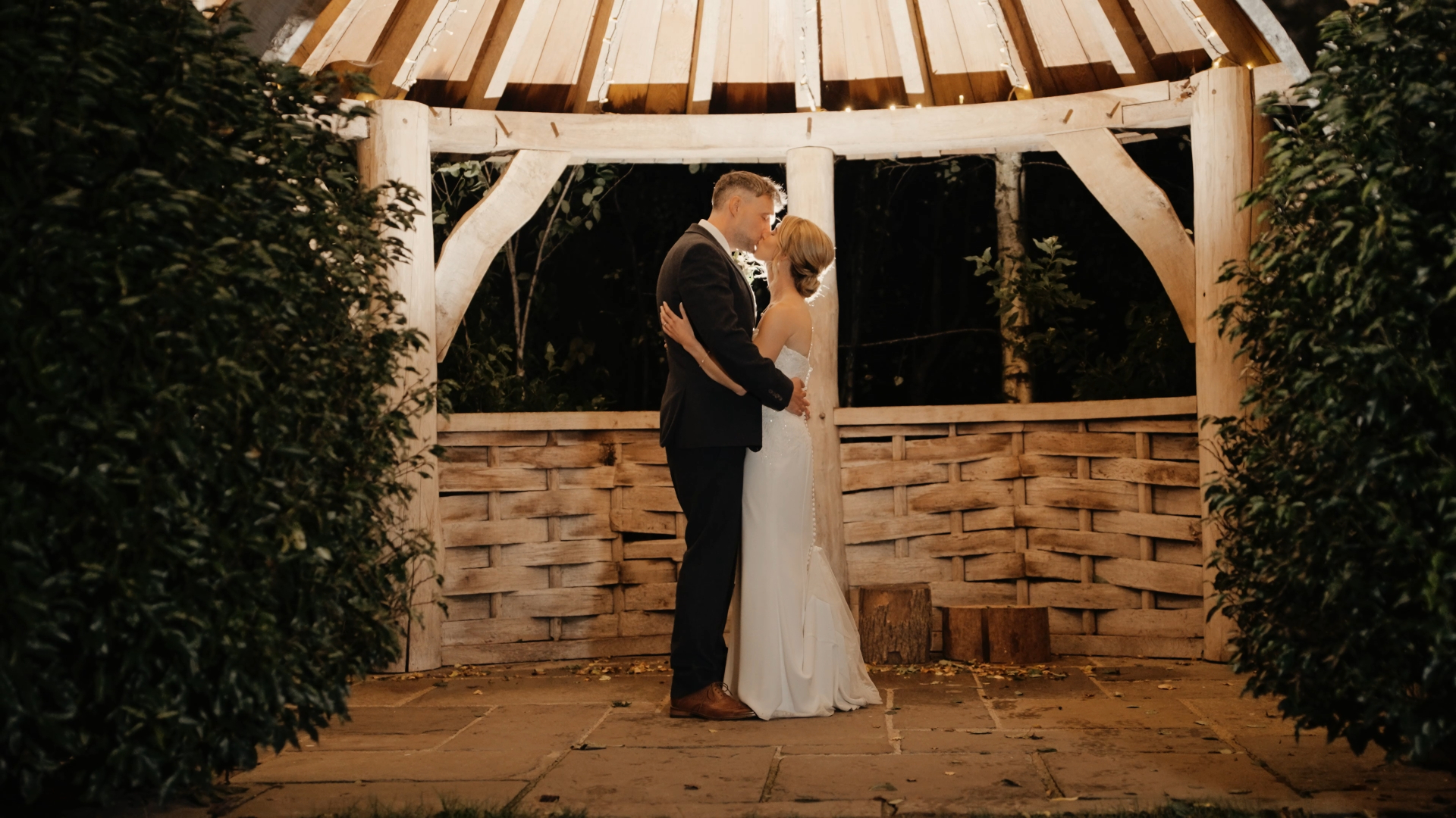 Bride and groom sharing a kiss under a roof adorned with glowing fairy lights, captured in a cinematic style, a trending wedding videography technique for 2025
