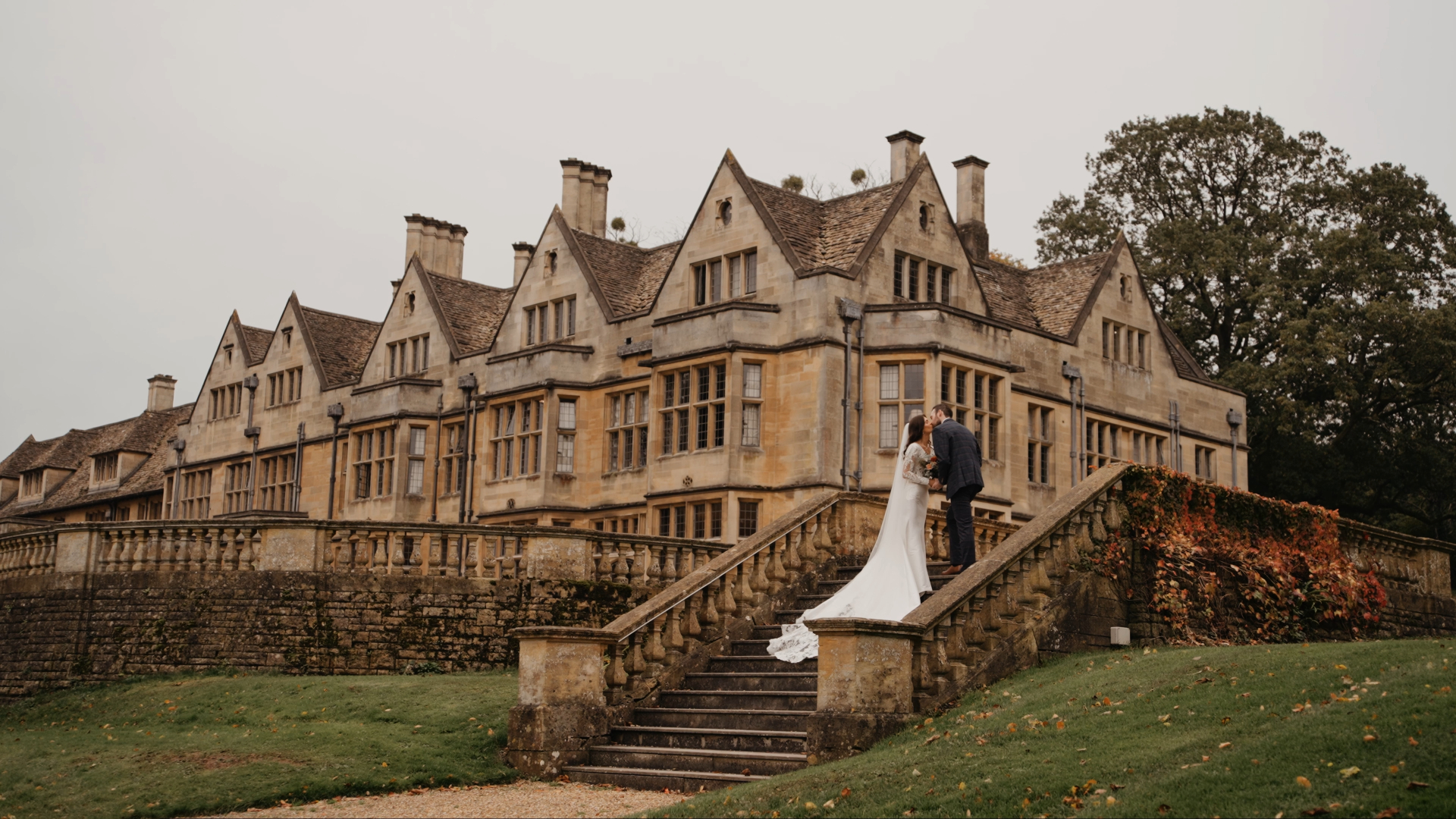 Bride and groom sharing a kiss on a stone staircase of a historic manor, captured by a Somerset wedding videographer during autumn.