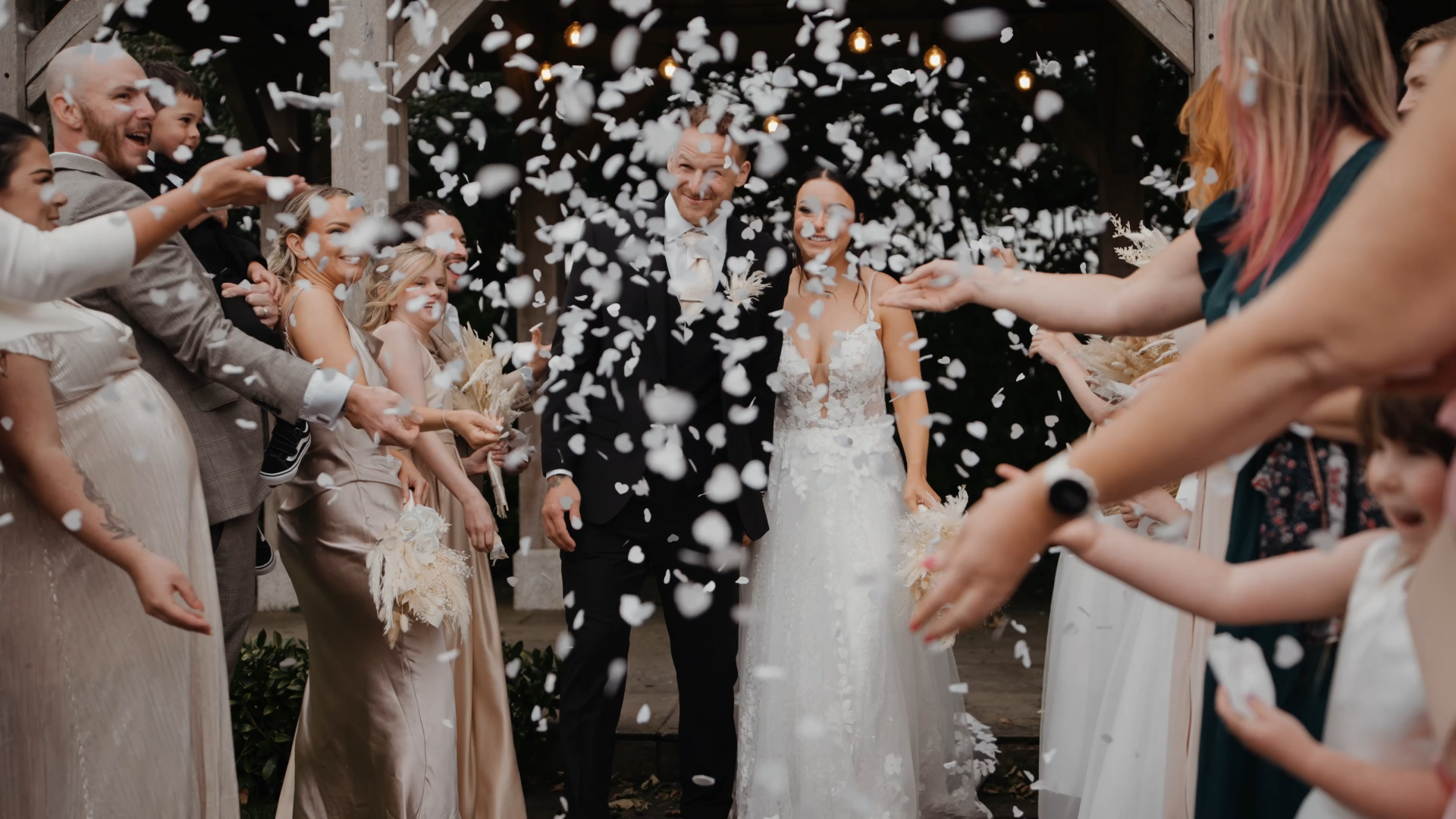  Bride and groom exiting the ceremony as smiling guests throw flower petals — a joyful and cinematic moment to capture in your wedding video by a Somerset wedding videographer