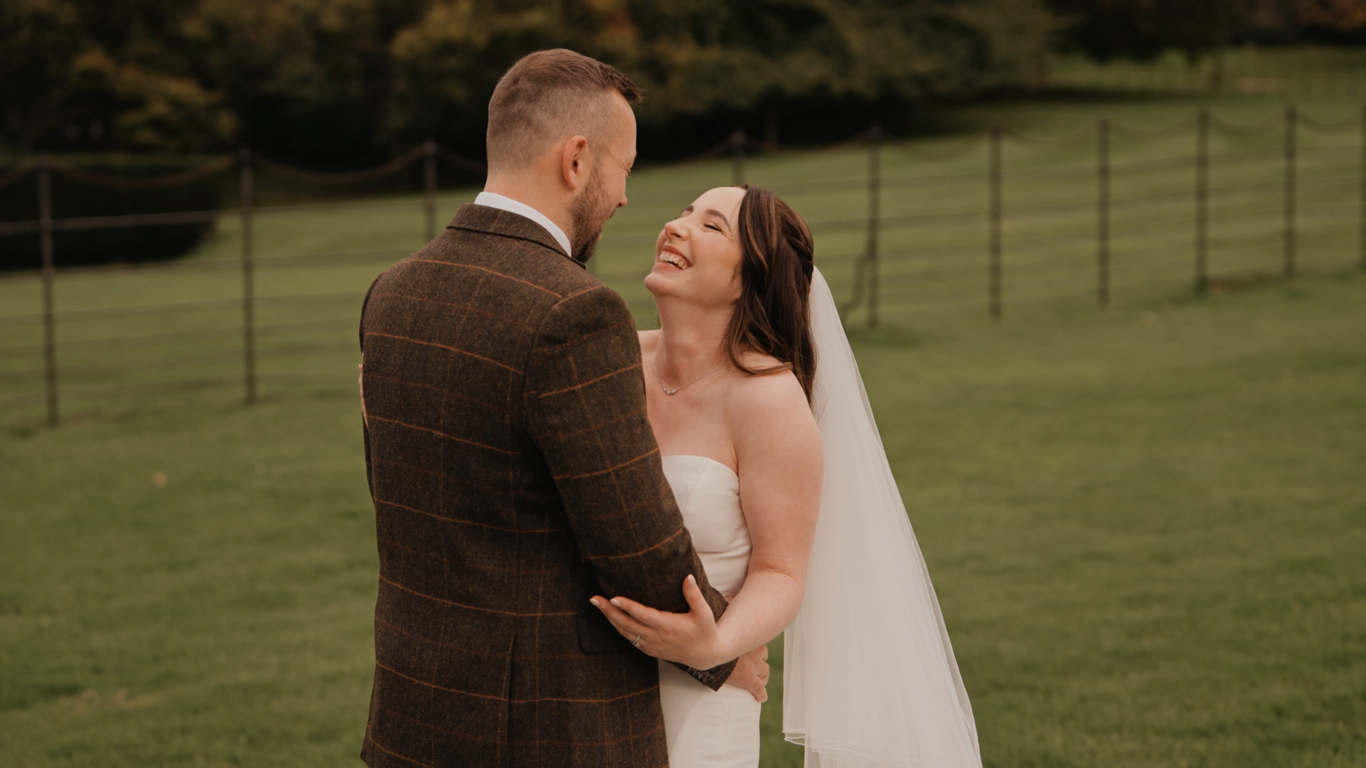 Bride smiling lovingly at the groom as they stand in a green field, a tender moment filmed by a Somerset wedding videographer.