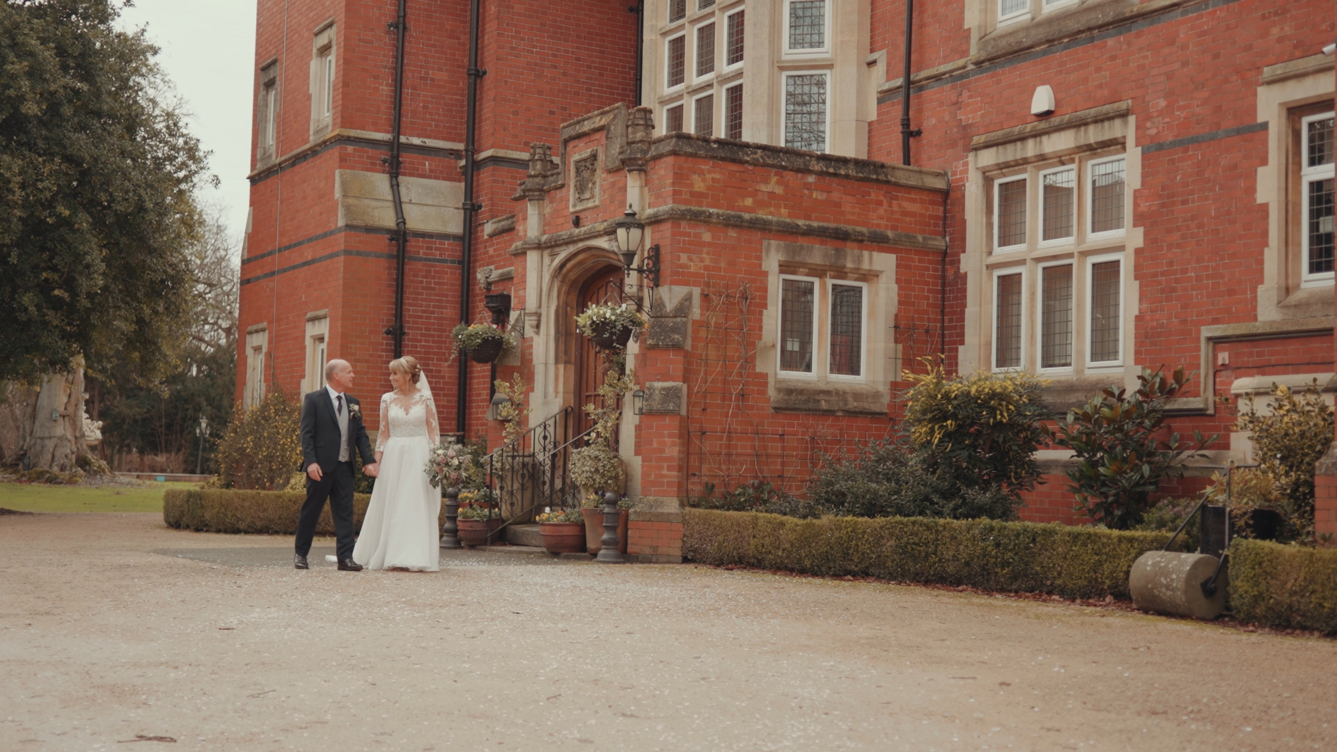 Somerset wedding videographer captures bride and groom walking hand in hand outside Berwicke Lodge, mid-conversation.