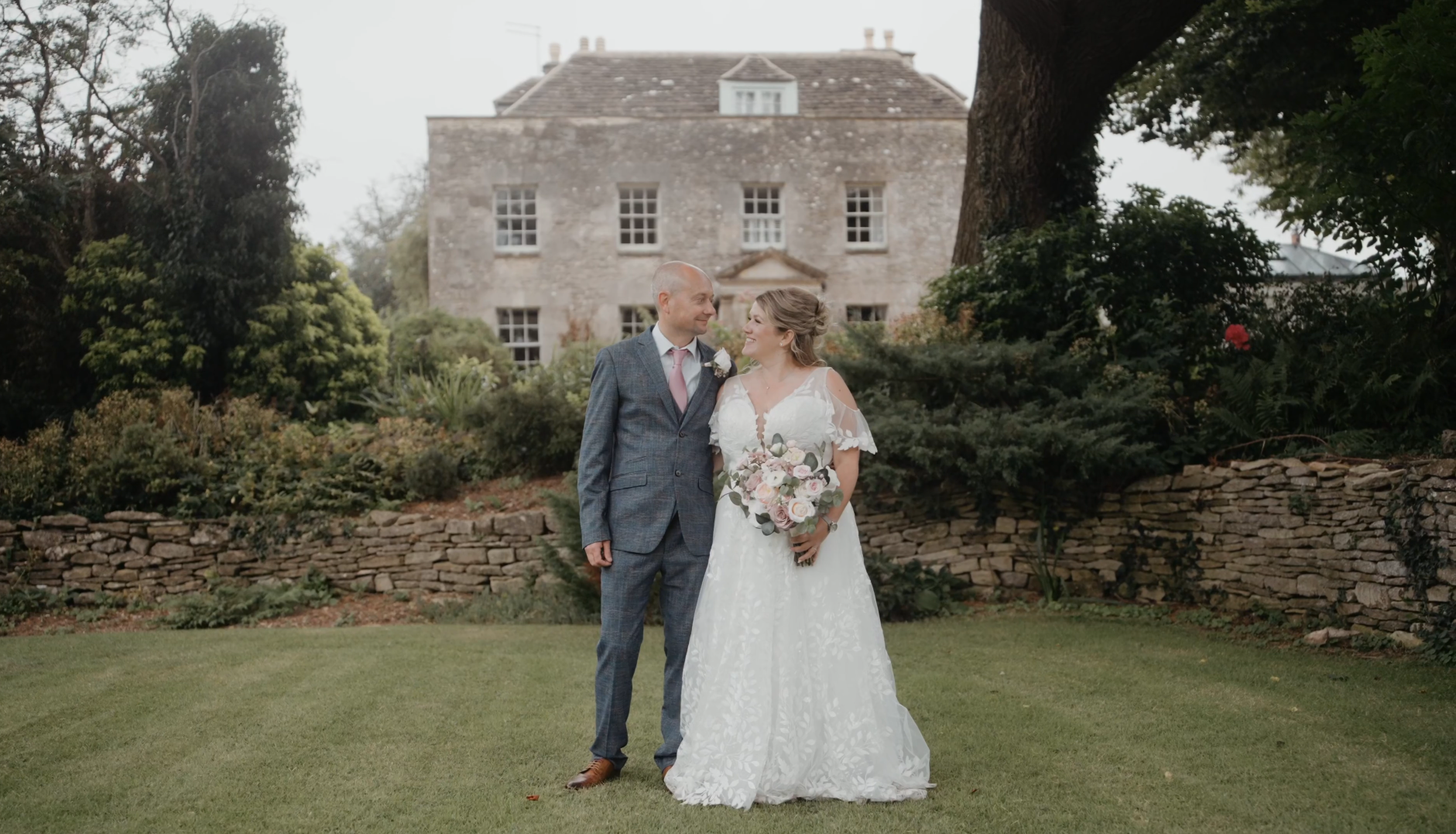 Bride and groom holding hands in a garden with a rustic house, capturing a romantic moment at a wedding venue in the South West.