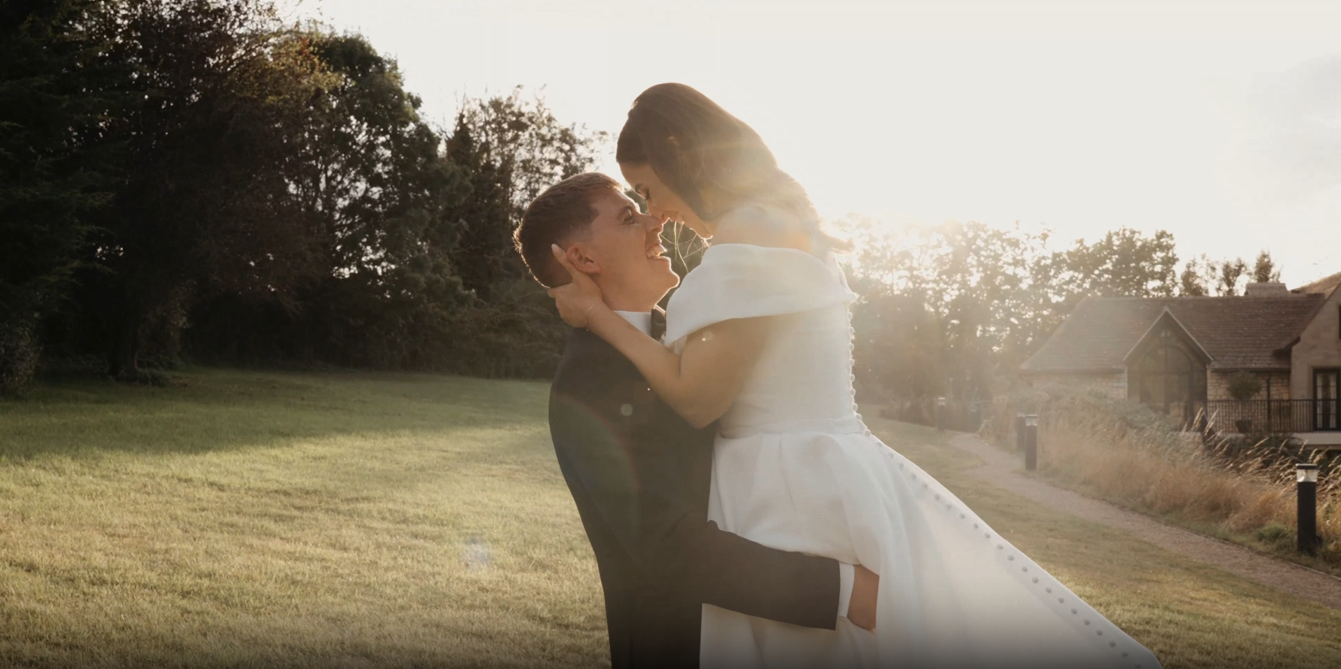Groom carries the bride in a glowing sunset field at The Pear Tree Purton, beautifully captured by a Somerset wedding videographer.