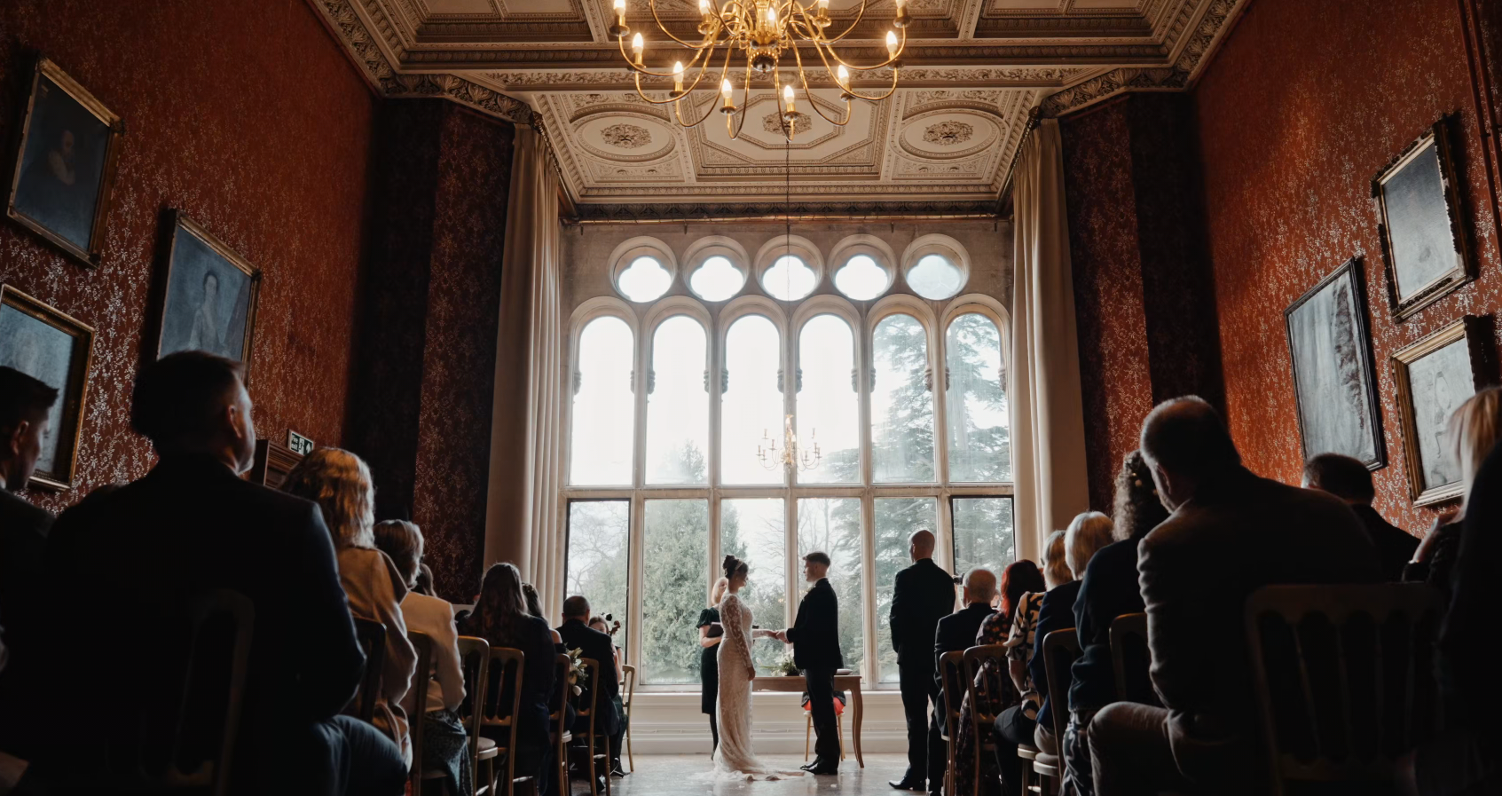 Bride and groom exchange vows in the elegant red gallery of Grittleton House, beautifully captured by a Somerset wedding videographer.
