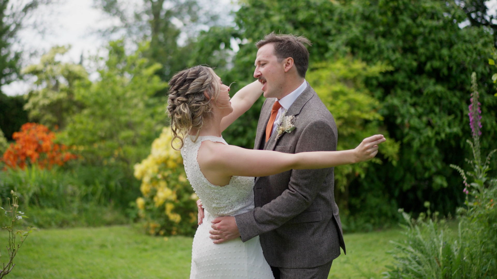 A couple dances joyfully in a lush garden, surrounded by vibrant flowers and greenery, beautifully captured in a documentary-style wedding video that highlights their authentic love and laughter.