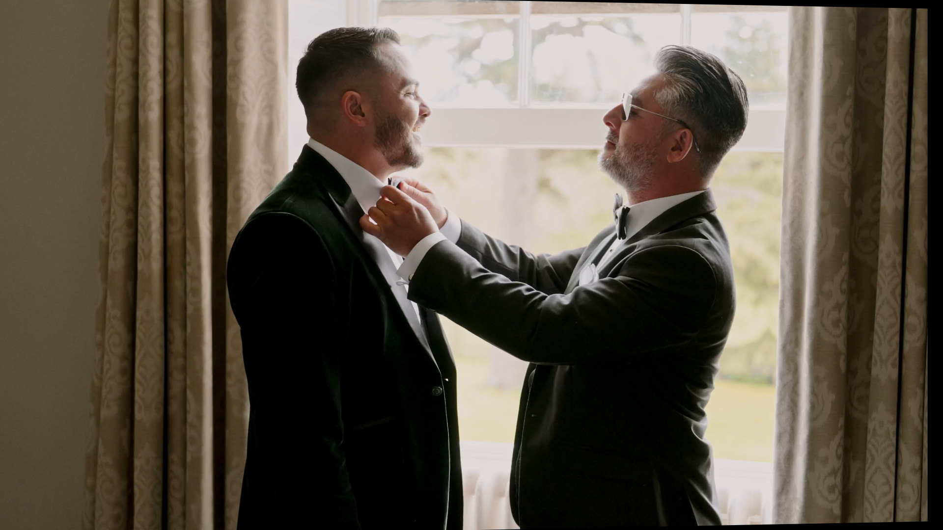The father of the groom gently adjusts his son's bow tie, a heartfelt and composed moment that highlights how to look your best on camera through personal touches and classic styling.