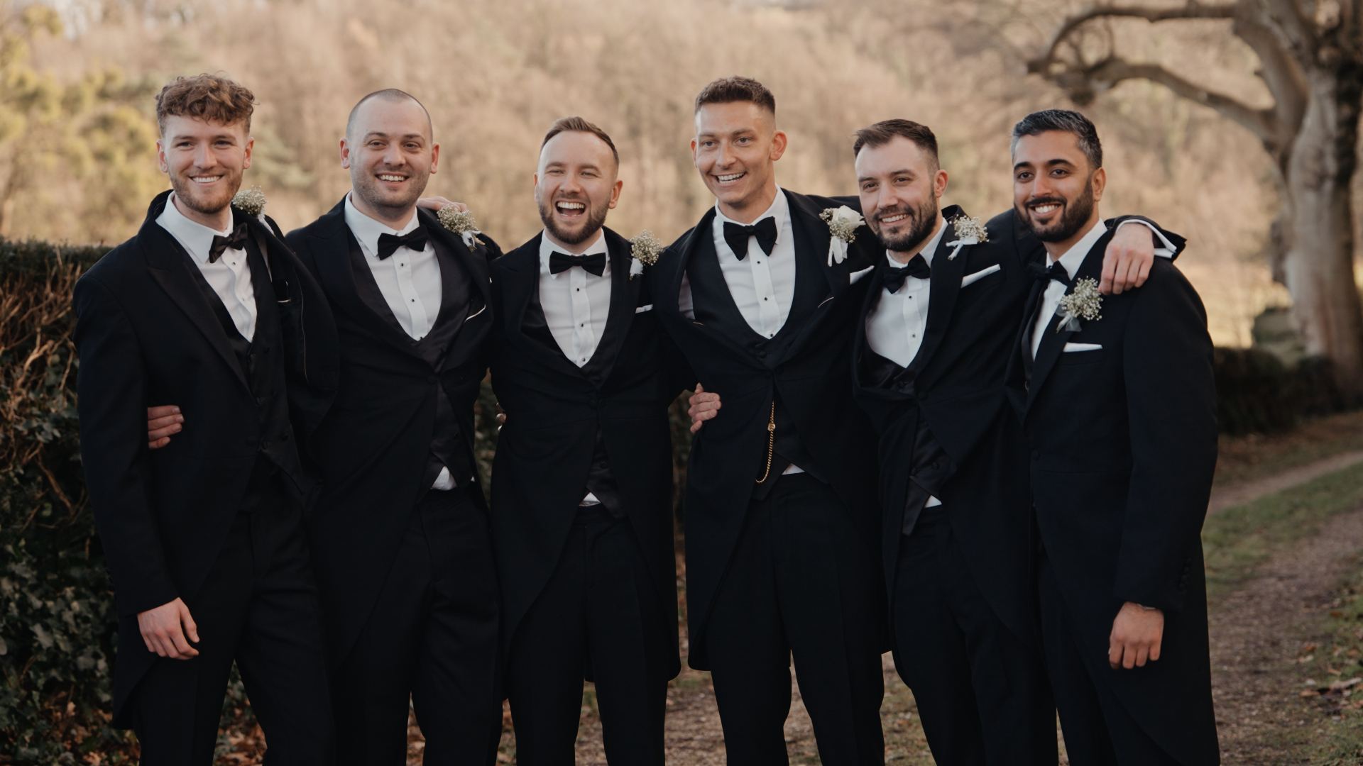 The groom and his groomsmen smile with their arms around each other’s shoulders, enjoying a lighthearted and memorable moment captured by the Best Wedding Videographer in the South West.