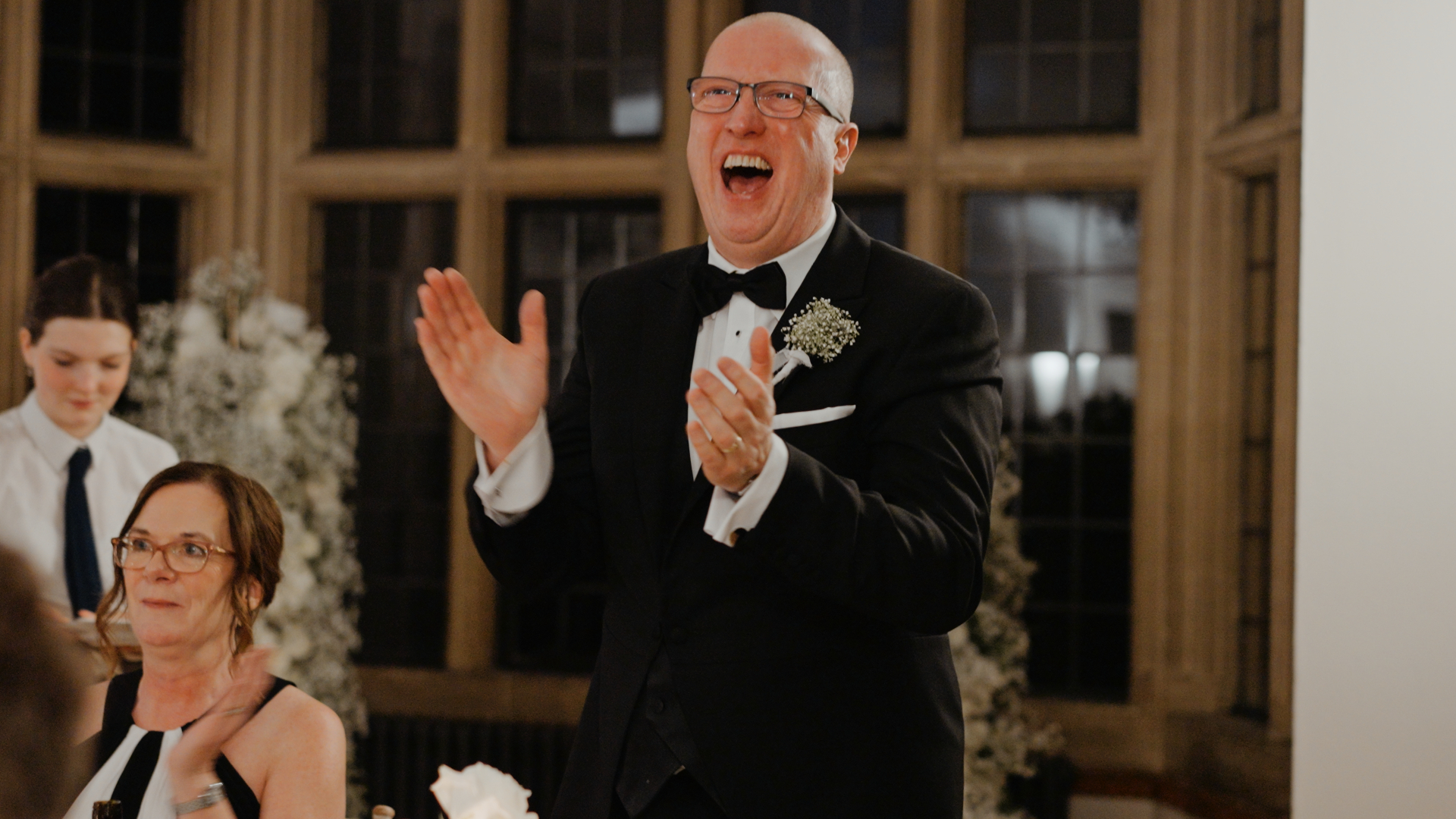 The father of the groom laughs and claps joyfully, a candid and expressive moment that shows how natural emotions help you look your best on camera.