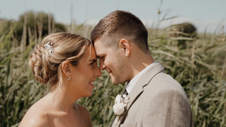 The bride and groom stand forehead to forehead, smiling warmly at each other, capturing a natural and flattering moment that shows how to look your best on camera.