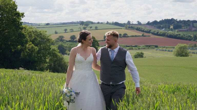 The bride and groom walk through an open field, smiling joyfully at each other, a heartfelt scene perfectly suited for their wedding video.