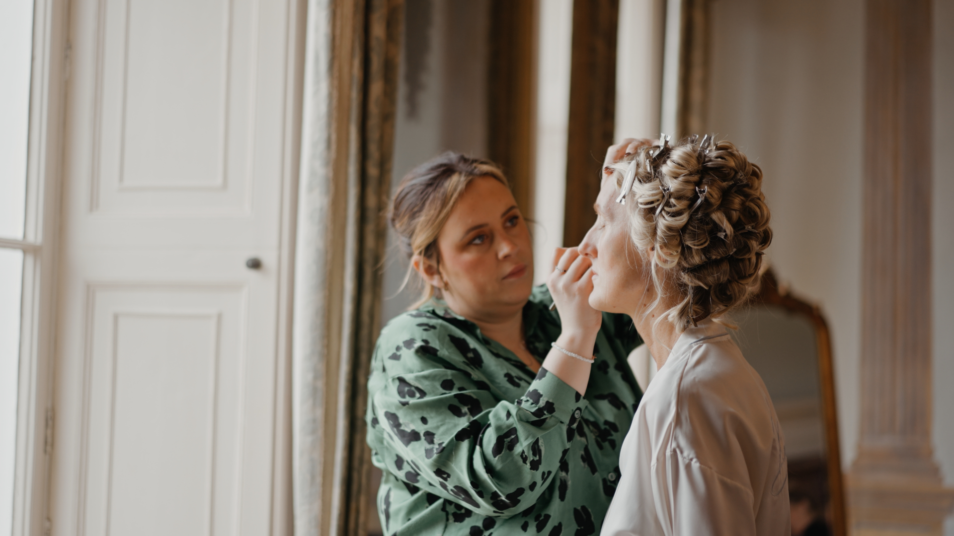 The bride getting her makeup done by a makeup artist, sitting calmly as final touches are applied—a behind-the-scenes moment that shows how to look your best on camera through professional preparation.