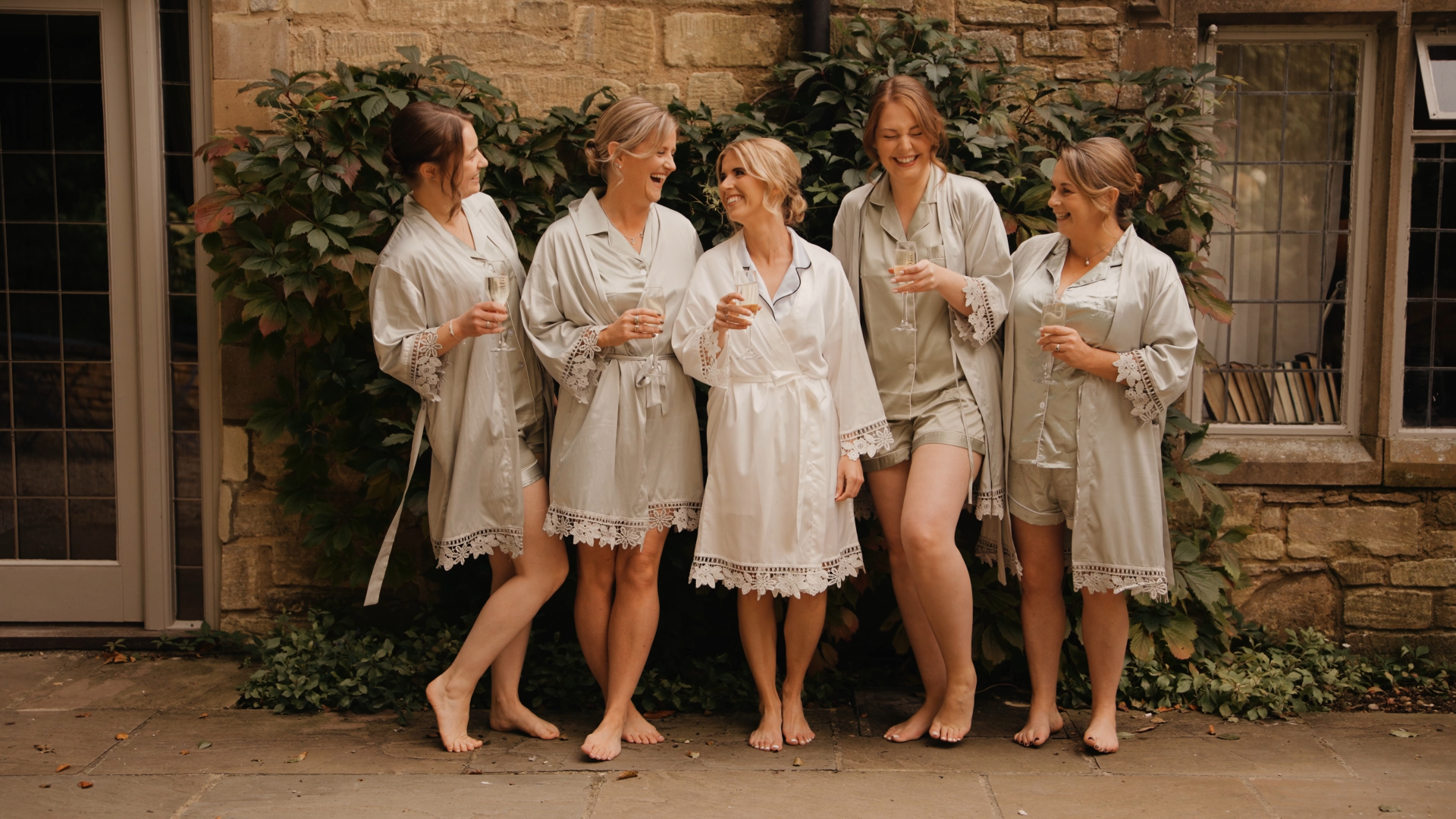 The bride and her bridesmaids in robes clinking champagne glasses in celebration, a joyful moment captured by the wedding videographer highlighting pre-ceremony excitement.