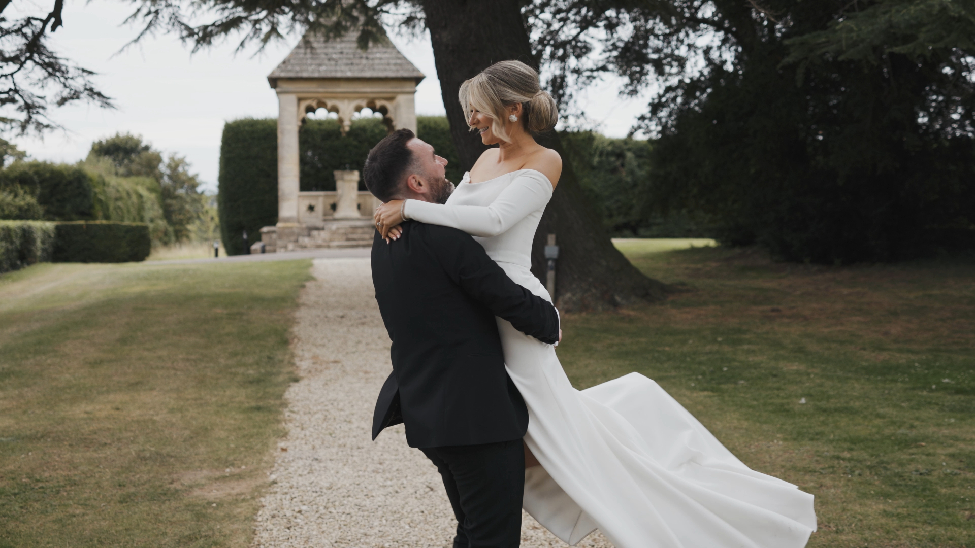 The groom carries the bride in his arms during their first dance, both smiling and laughing, creating a romantic and playful highlight for their wedding video.