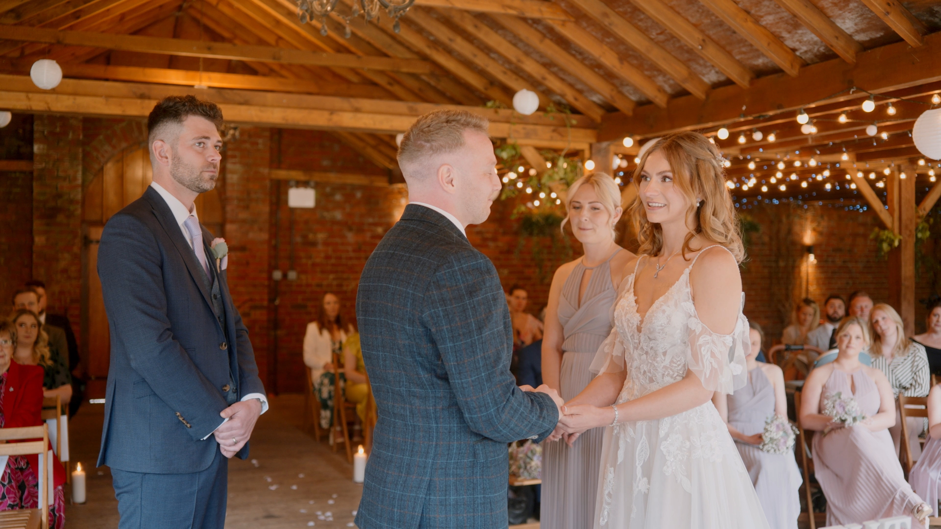 A bride and groom holding hands while saying their emotive wedding vows in a rustic venue adorned with warm fairylights, creating an intimate and romantic atmosphere.