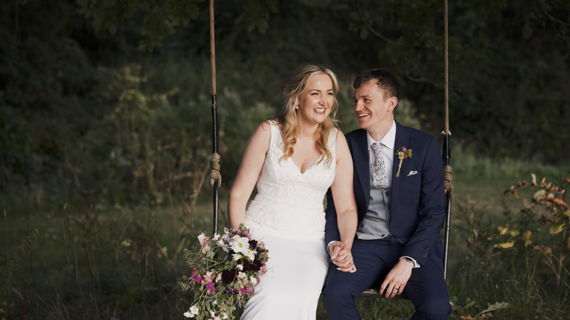 A bride and groom sitting together on a tree swing in a peaceful forest in Somerset, sharing an intimate moment during their elopement, surrounded by greenery and soft natural light.