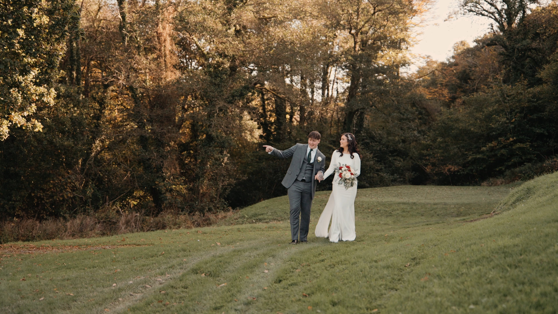 The bride and groom walk hand in hand through a wide, open field, surrounded by natural beauty—an idyllic and cinematic scene for their wedding video.