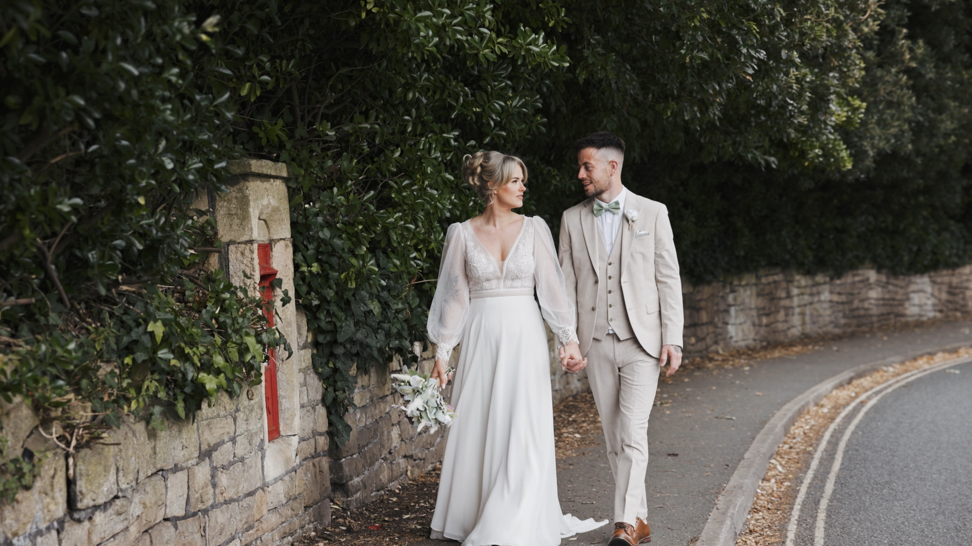 The bride and groom walk hand in hand along a charming sidewalk, sharing a quiet and intimate moment beautifully filmed by the Best Wedding Videographer in the South West.