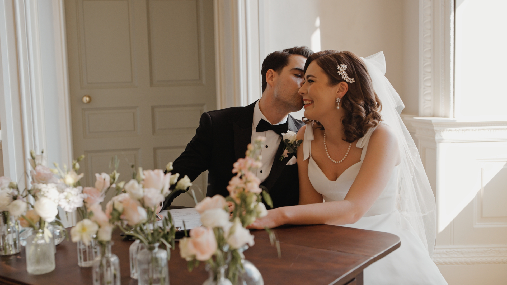 The groom tenderly kisses the bride’s cheek, capturing a sweet and intimate moment through the lens of the wedding videographer.

