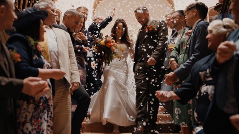 Guests throw flower petals at the bride and groom as they joyfully exit the wedding venue, a moment full of movement and emotion that can often be missed due to common wedding videography mistakes like poor timing or framing.