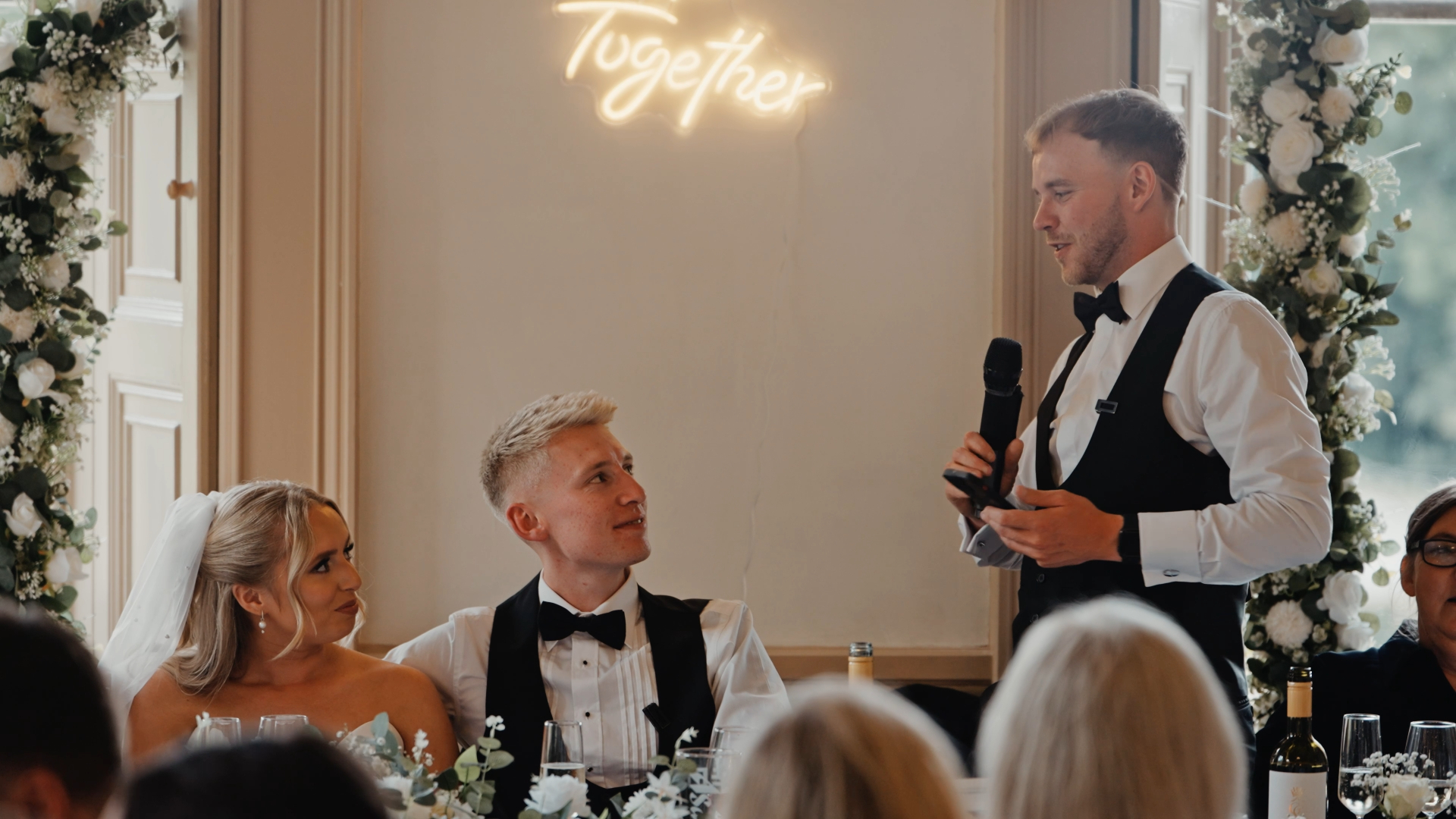 
The best man giving a heartfelt speech while facing the newlyweds during the wedding reception, a key moment that can be compromised by common wedding videography mistakes such as poor audio capture or awkward camera angles.