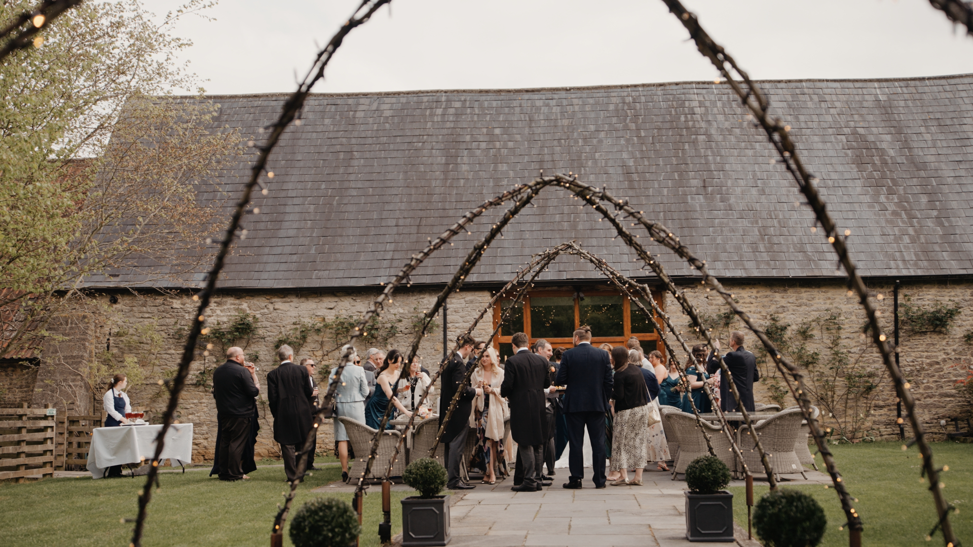 
Guests socializing and enjoying drinks during cocktail hour outside the wedding venue, surrounded by seasonal blooms and natural light, capturing the relaxed elegance of a seasonal wedding.
