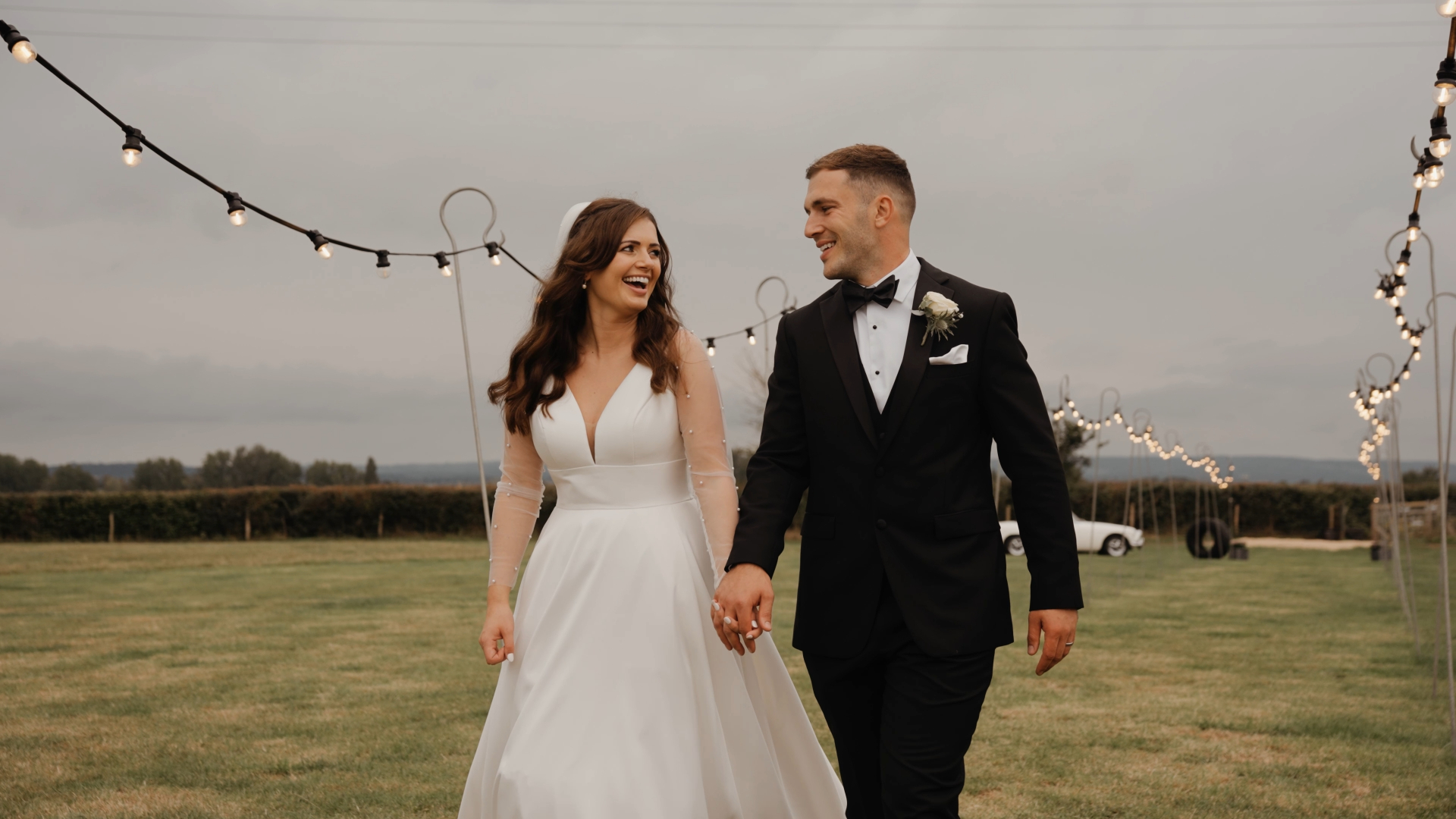 The bride and groom smiling at each other as they walk hand in hand through a scenic field, a beautifully candid moment that benefits from stable camera movement—often overlooked in common wedding videography mistakes.