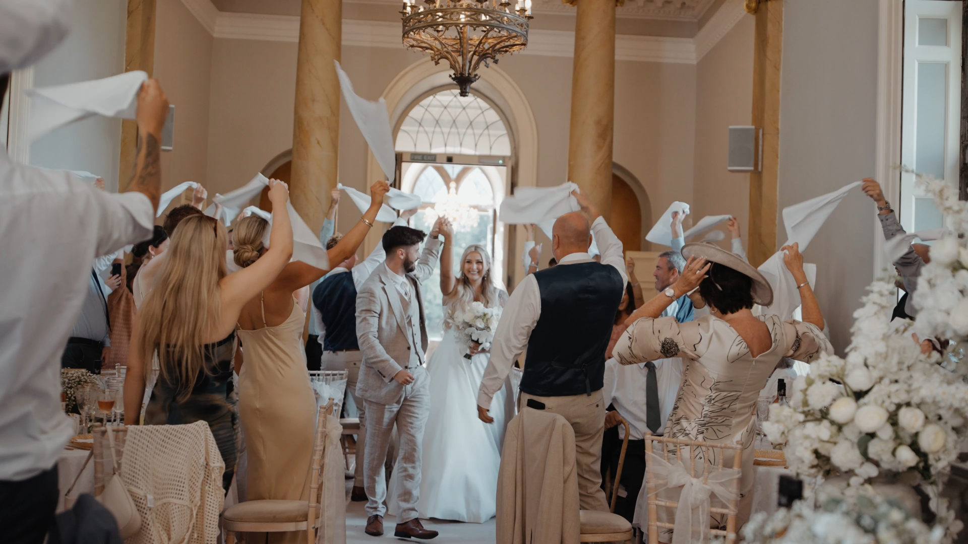 
Guests enthusiastically waving their napkins in the air during the wedding reception while the bride and groom smile and laugh, a joyful moment that can be diminished by common wedding videography mistakes like shaky footage or missed reactions.