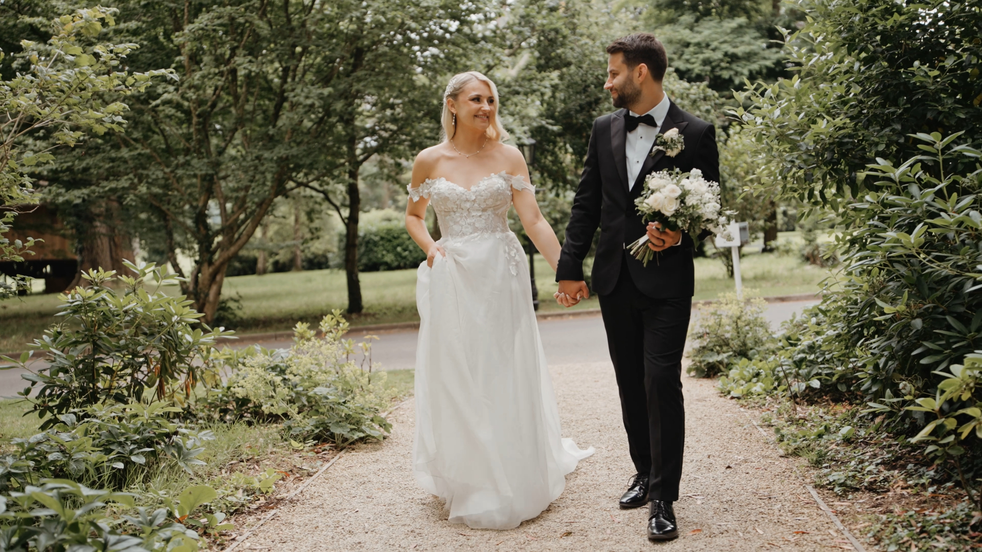 
The bride and groom walking together in a sunlit garden, bathed in bright natural light, surrounded by lush greenery—a radiant moment that beautifully reflects the essence of a seasonal wedding.