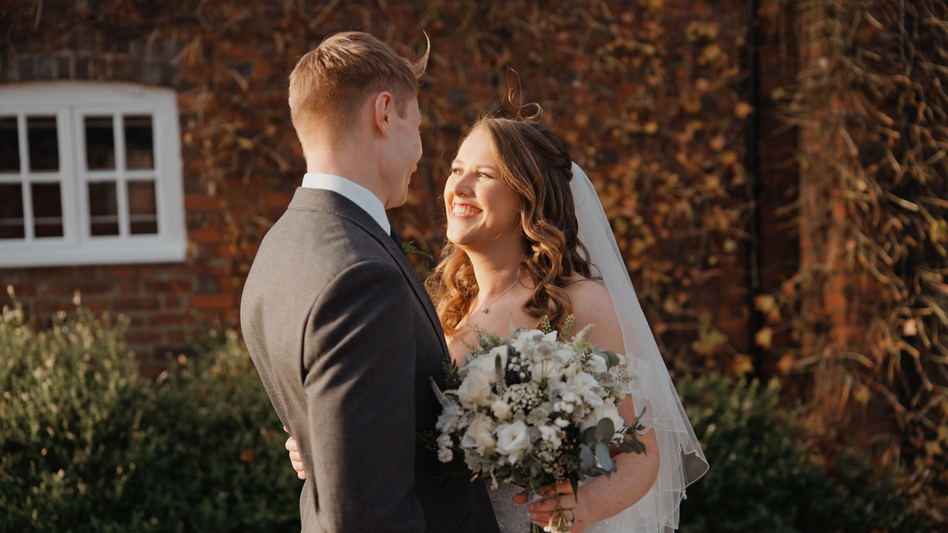 The bride smiles warmly at the groom as sunlight gently illuminates her face, capturing a glowing and emotional moment by the Best Wedding Videographer in the South West.
