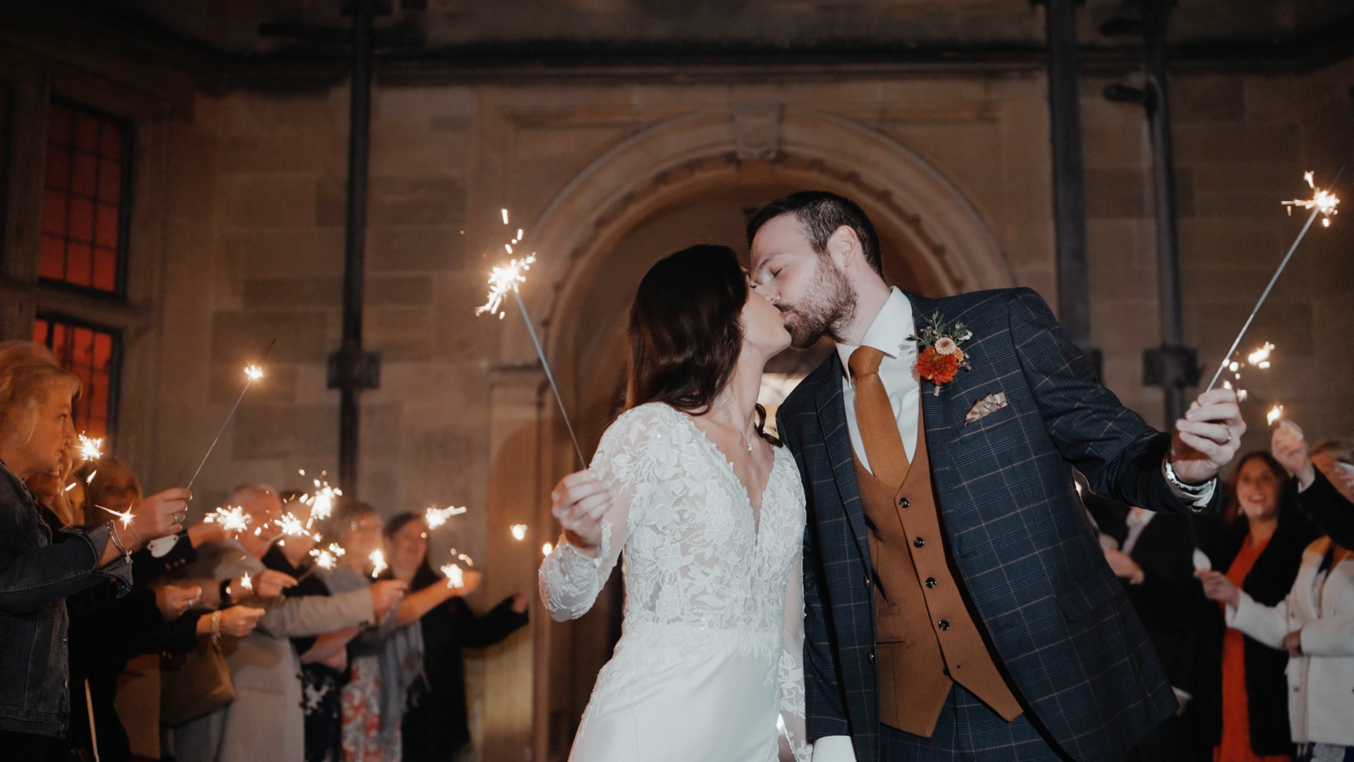 The bride and groom kiss while holding out sparklers, creating a magical and sparkling moment beautifully captured by the wedding videographer.

