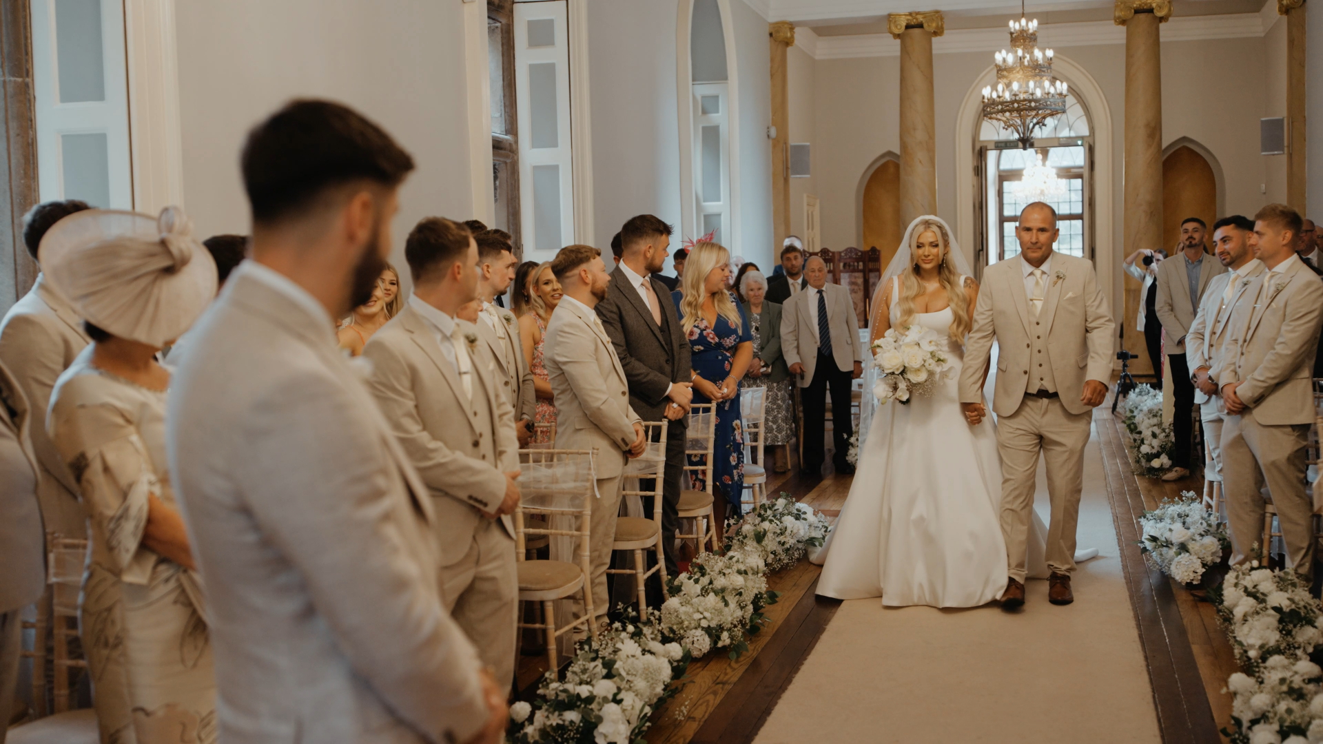 The groom gazes lovingly at the bride as she walks down the aisle with her father, a heartfelt and emotional moment beautifully captured by the Best Wedding Videographer in the South West.