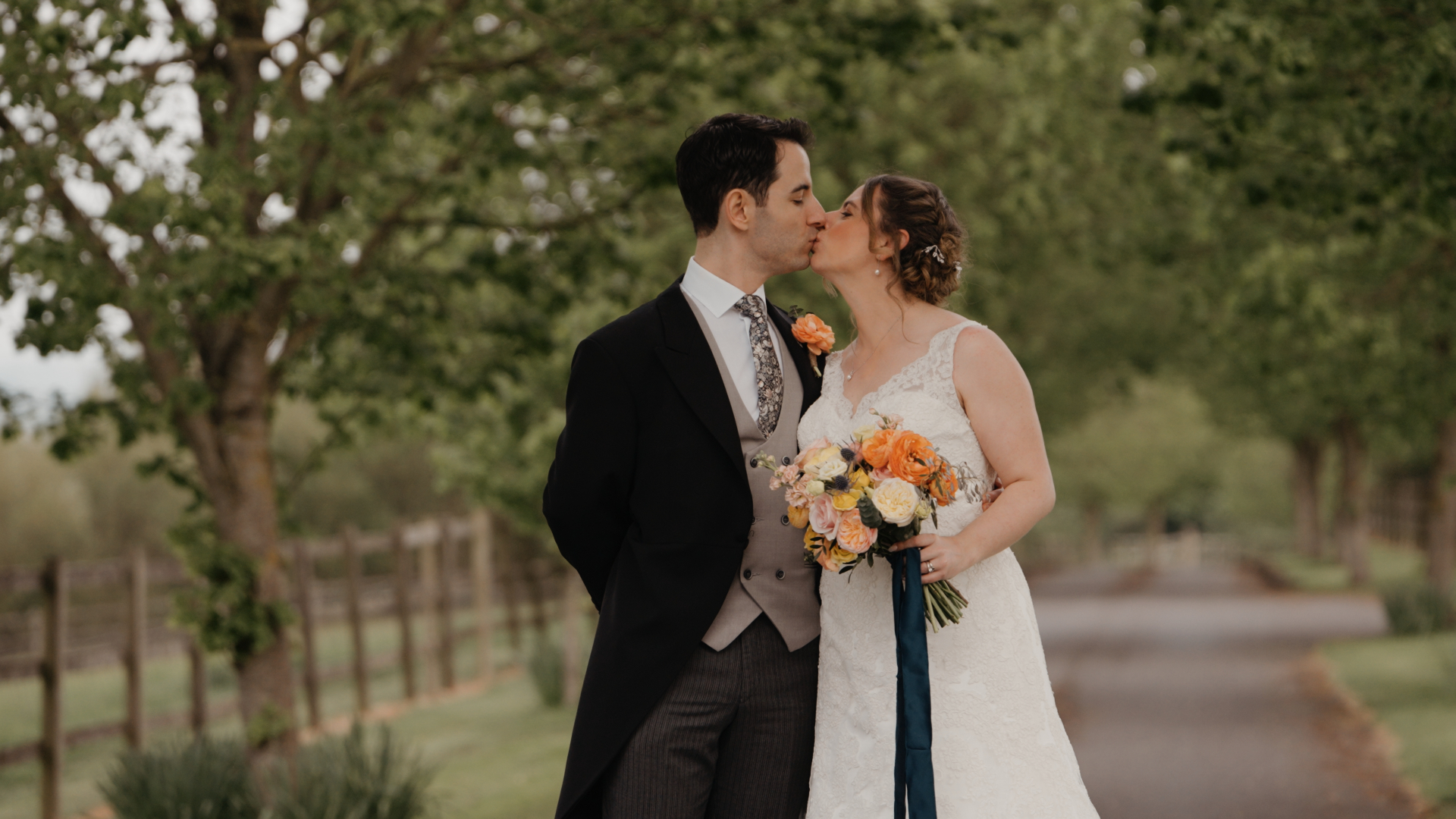 The bride kisses the groom while holding a vibrant orange and yellow bouquet, capturing a warm and colorful moment beautifully filmed by the Best Wedding Videographer in the South West.