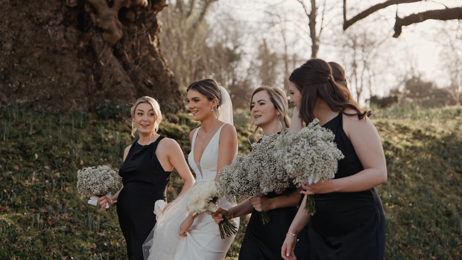 The bride and her bridesmaids laugh together as they walk through a forest path, sharing a joyful and candid moment beautifully captured by the Best Wedding Videographer in the South West.